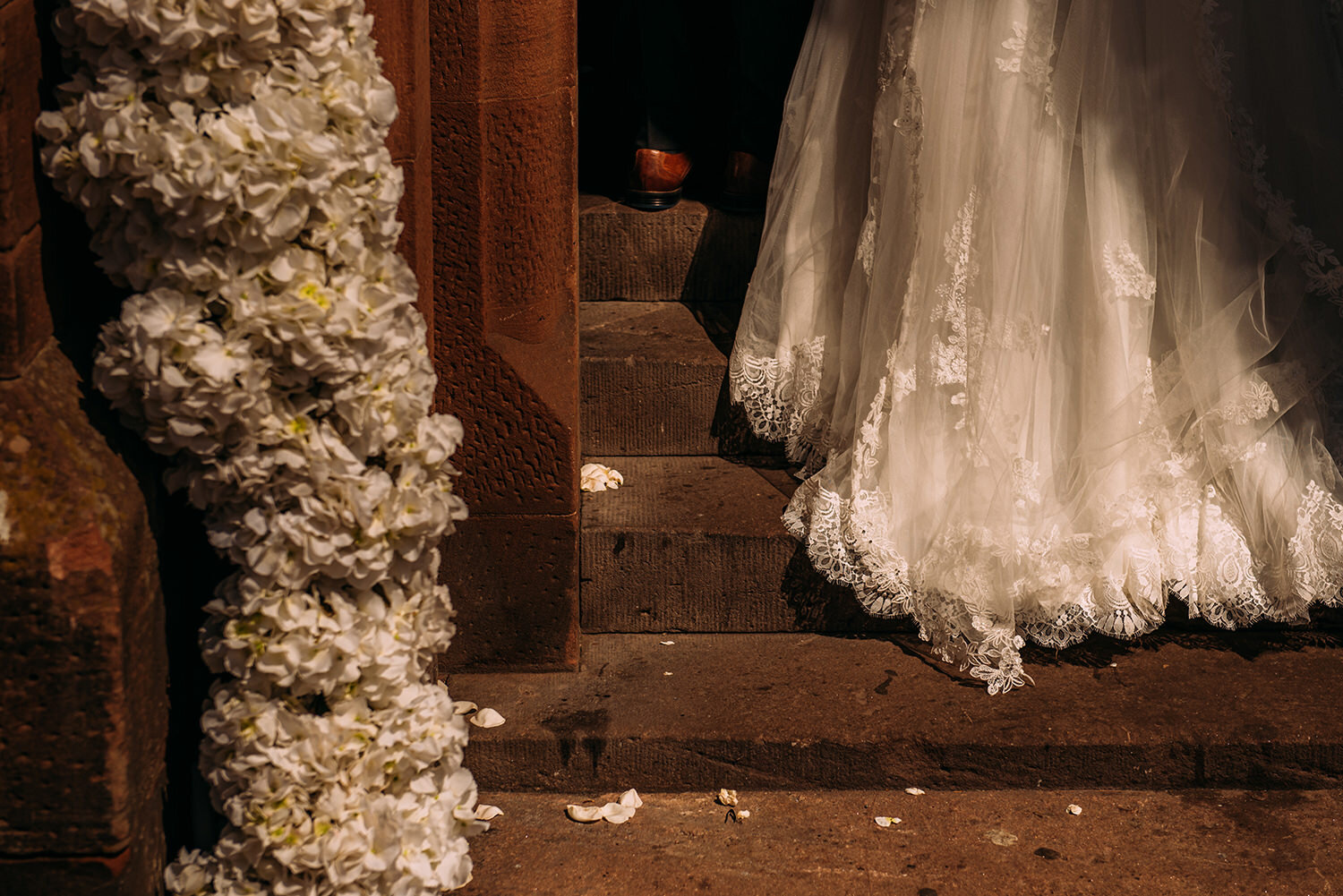  detail of brides dress as she walks up steps past flowers 