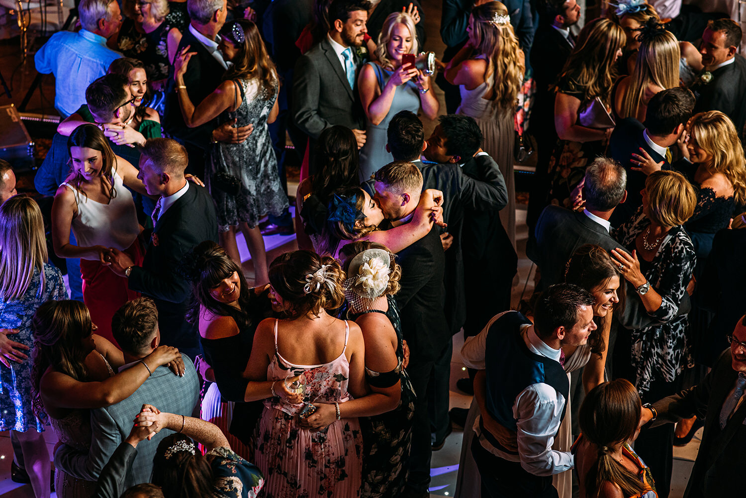  Packed dance floor from above with a couple kissing in the middle. 