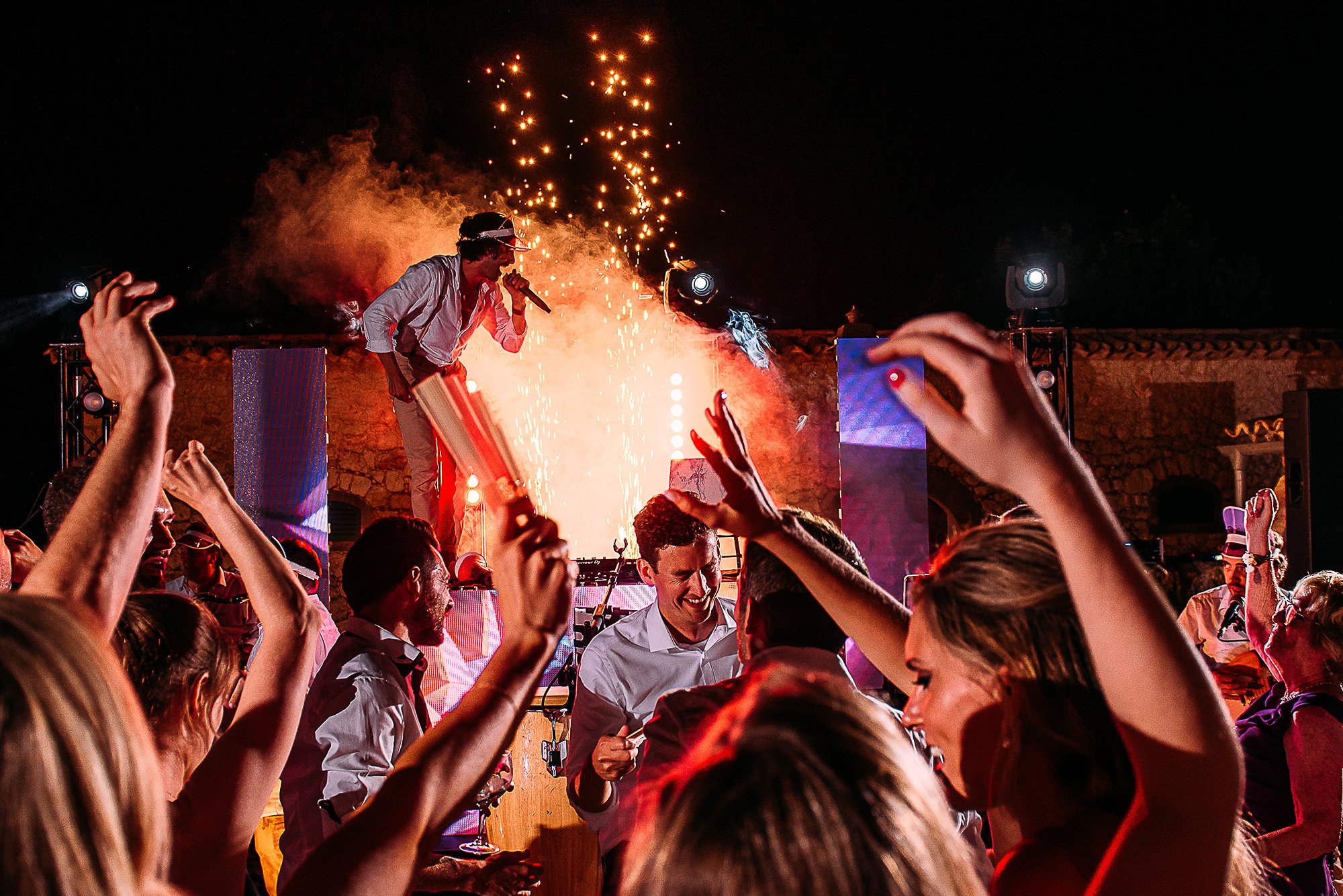  Wedding DJ standing on decks with mic in front of sparks and the crowd. 