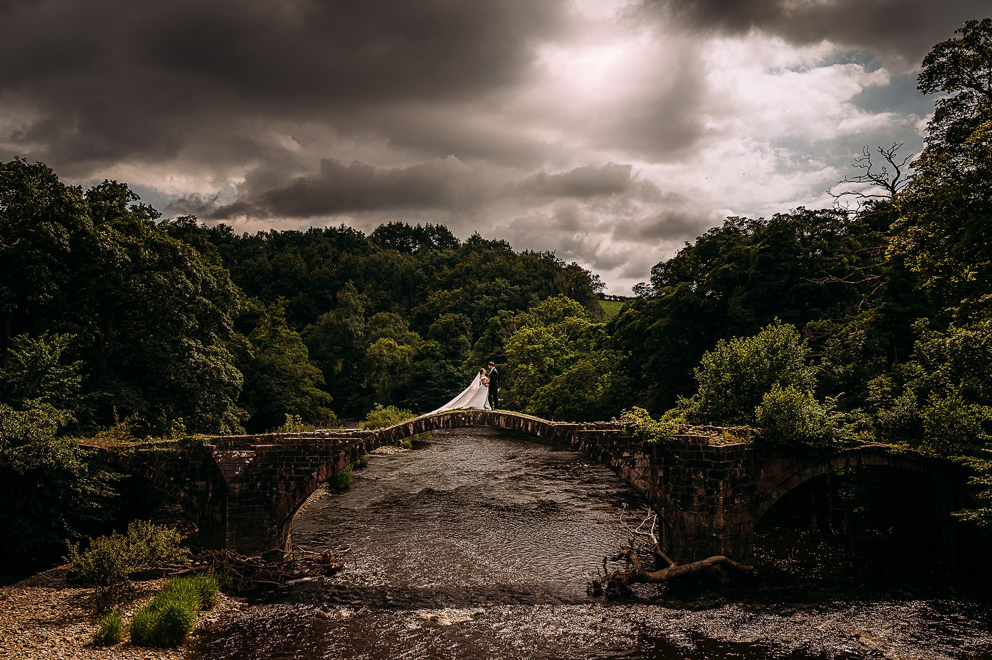  Bride and groom standing on an old bridge over a river. 