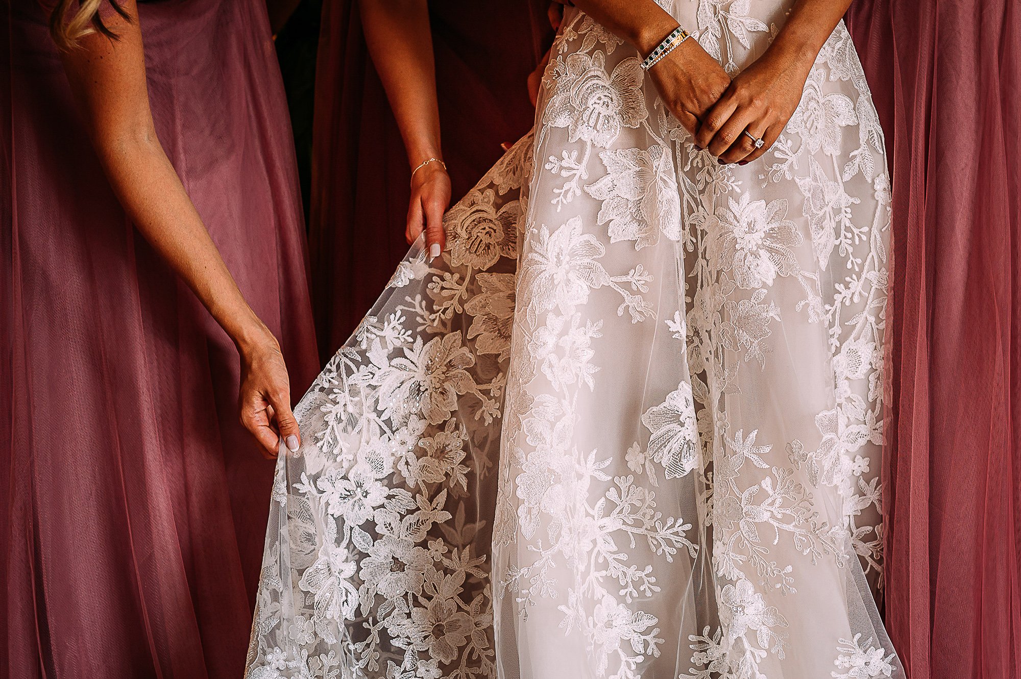  Detail shot of the bridesmaid in pink dress adjusting the brides dress. 