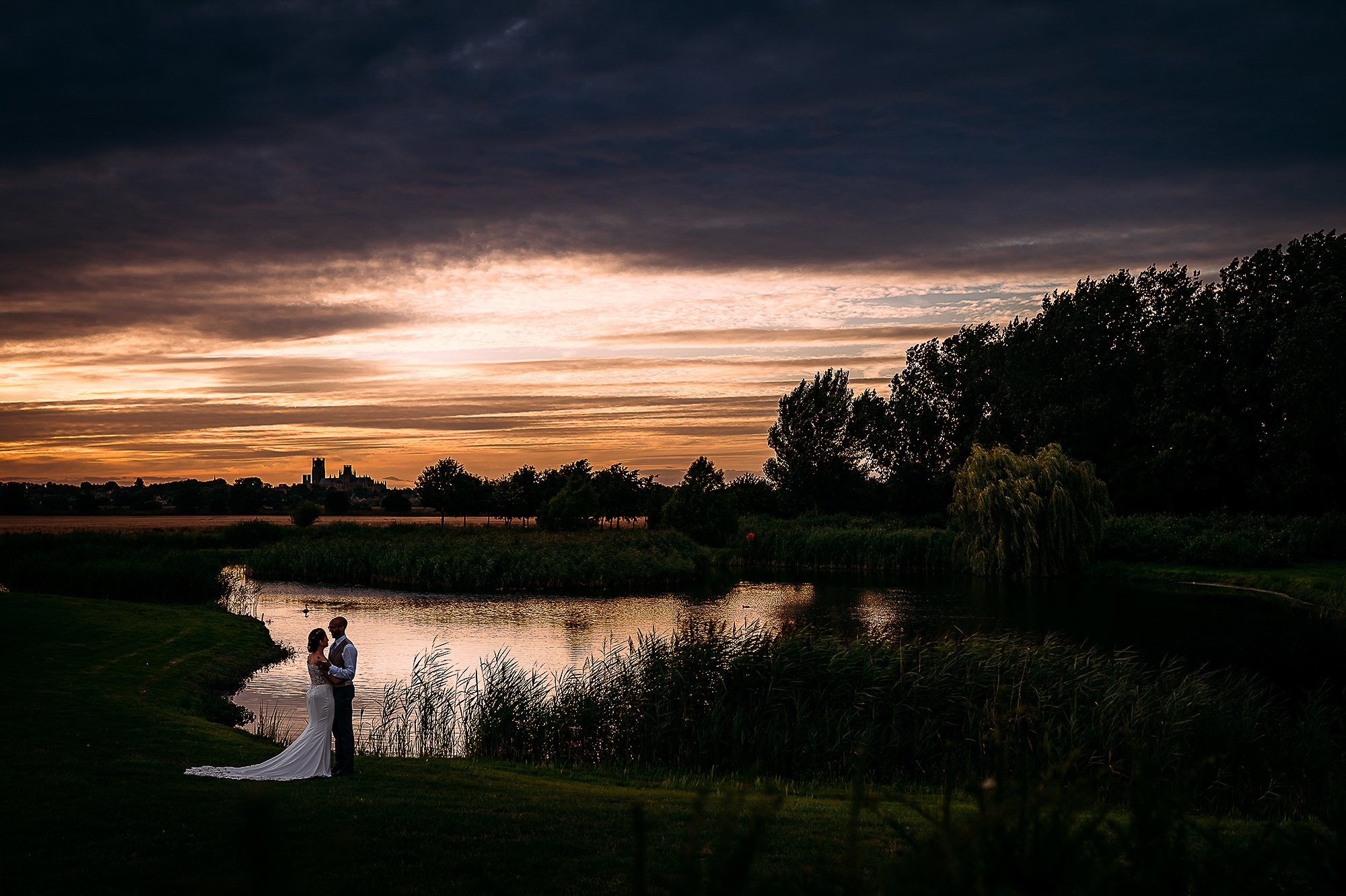  Couple silhouette by a lake with a backdrop of Cambridge. 
