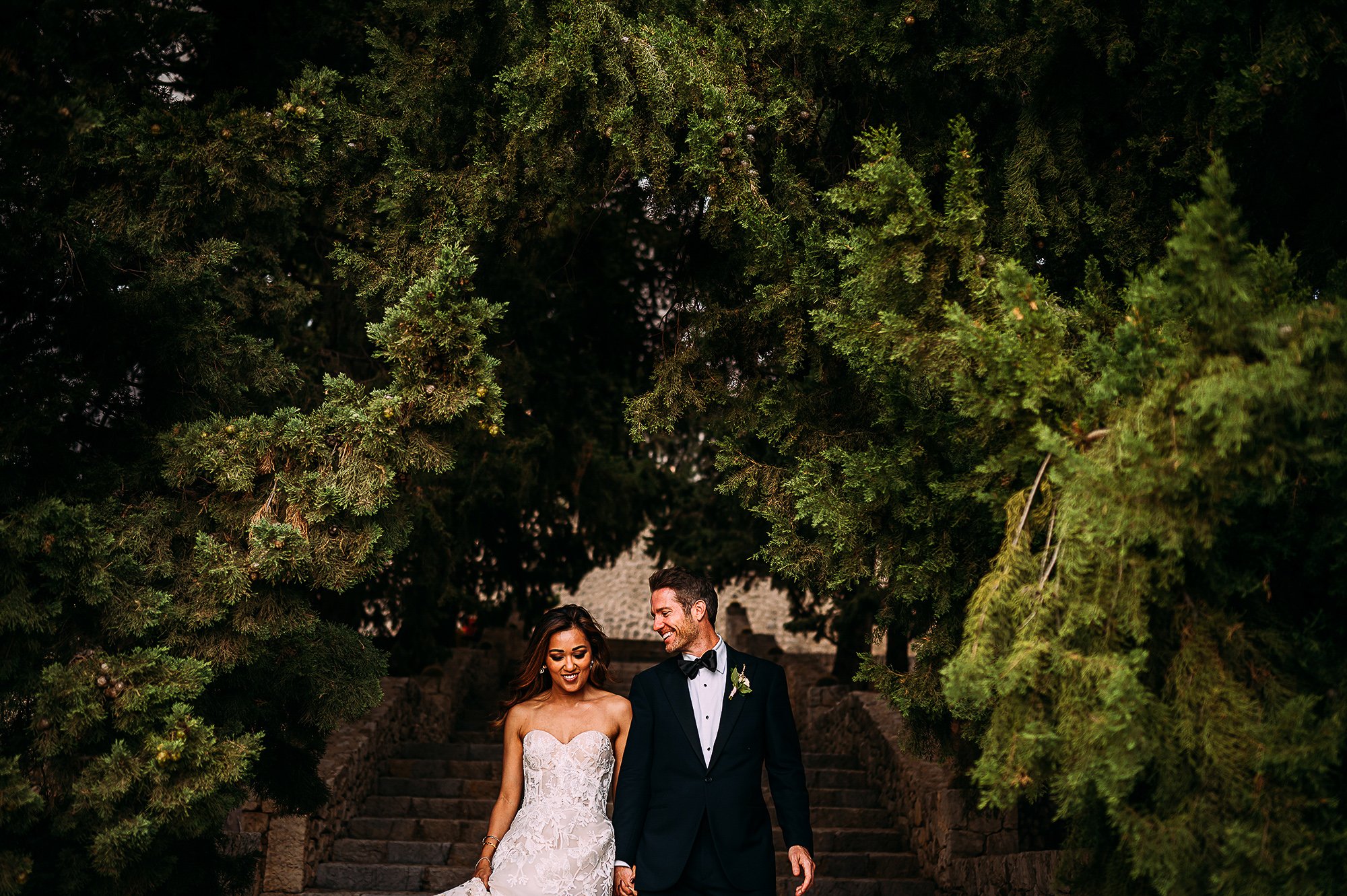  Couple walking down stairs under green trees in Mallorca. 
