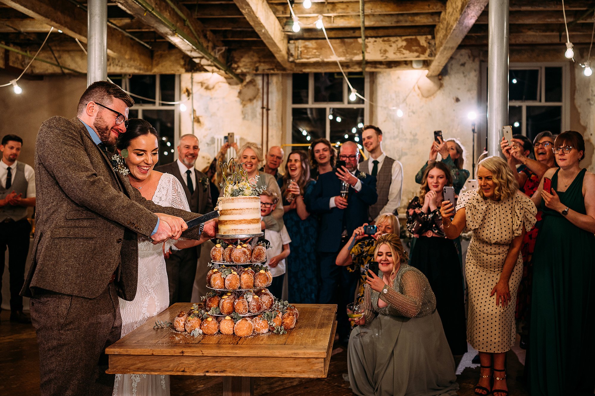  Couple cutting cake in front of guests at Holmes mill. 