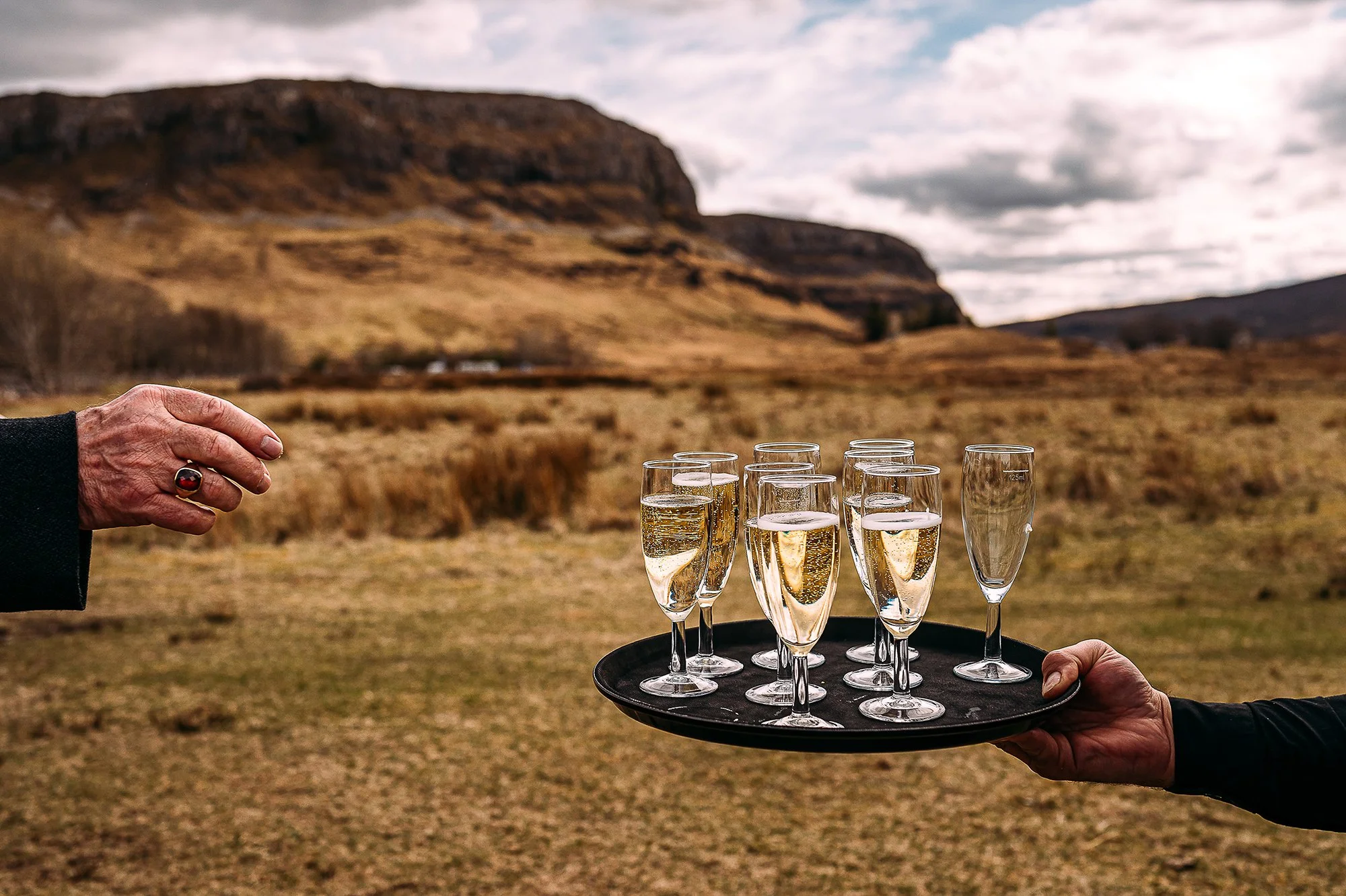 Detail of a hand reaching for champagne in front of Highland hills.