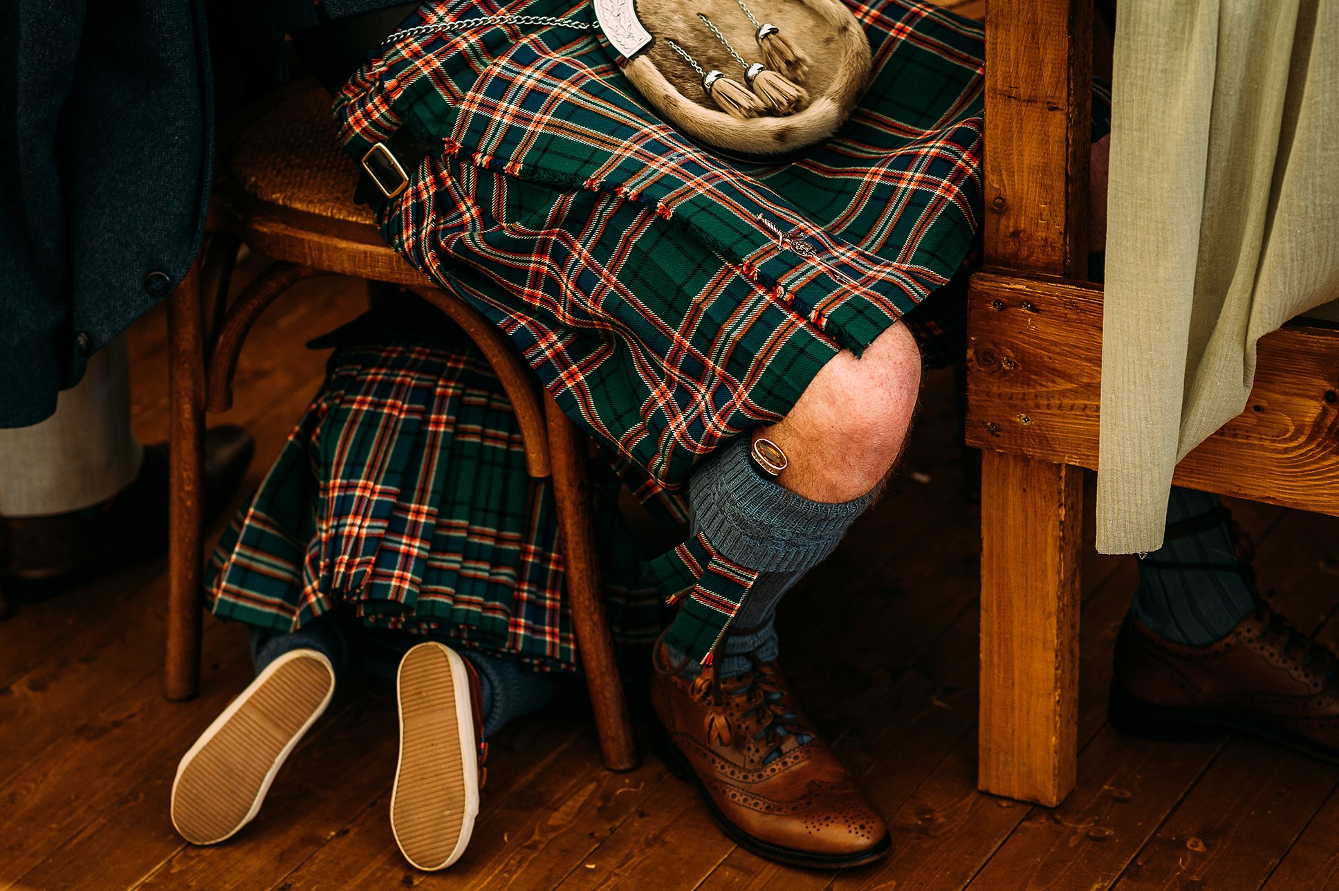  Close up of son hiding under dads chair. Both wearing matching kilts. 