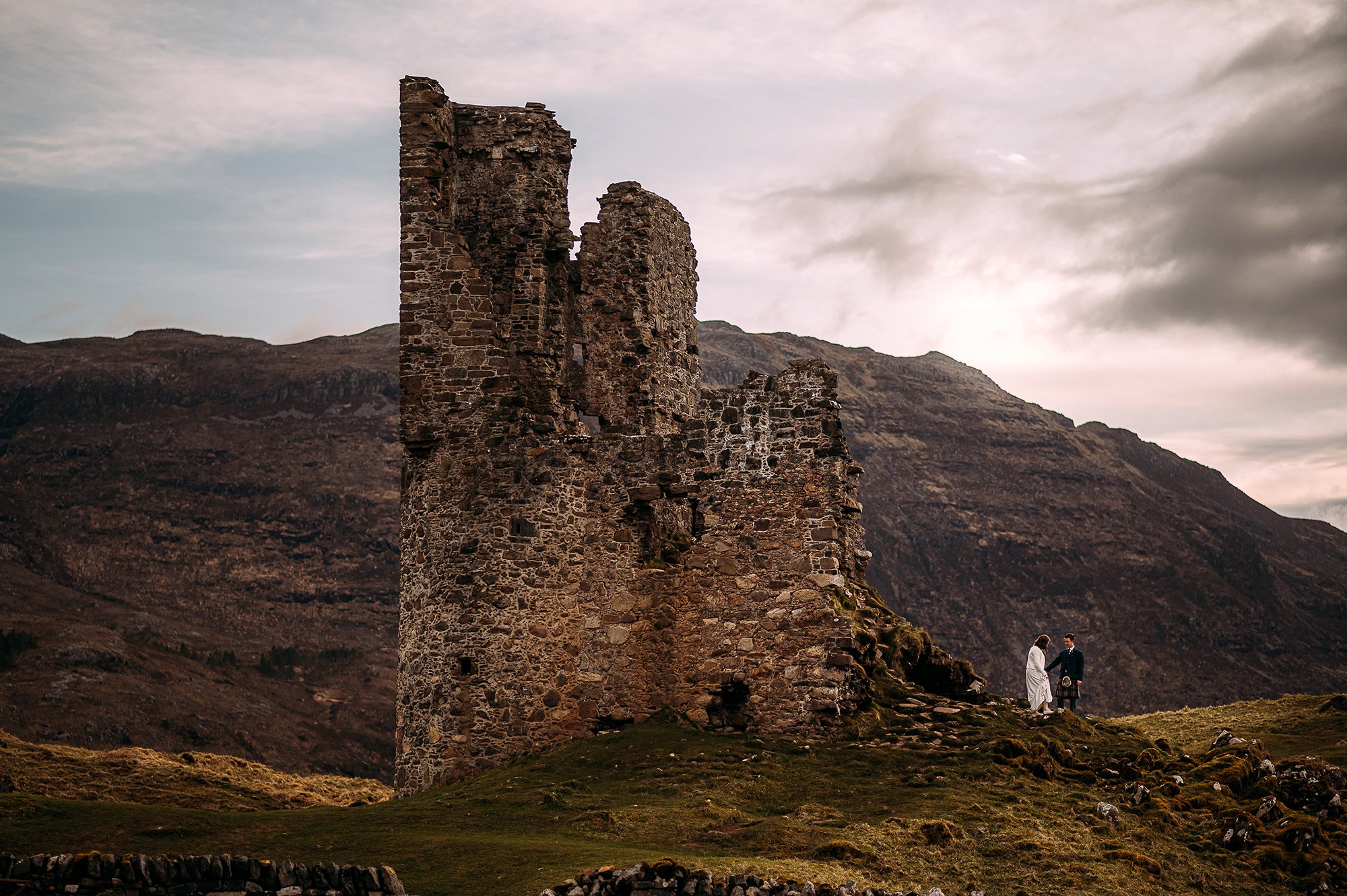  Bride and groom next to old ruins in the Scottish highlands. 
