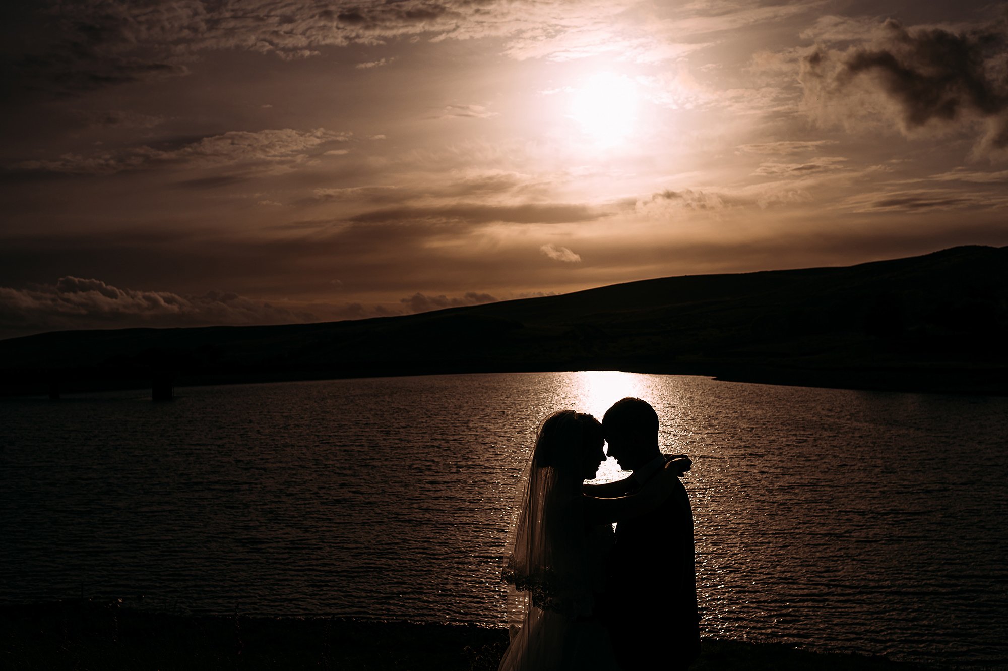  Sunset silhouette of a couple in the sun reflection on a lake. 