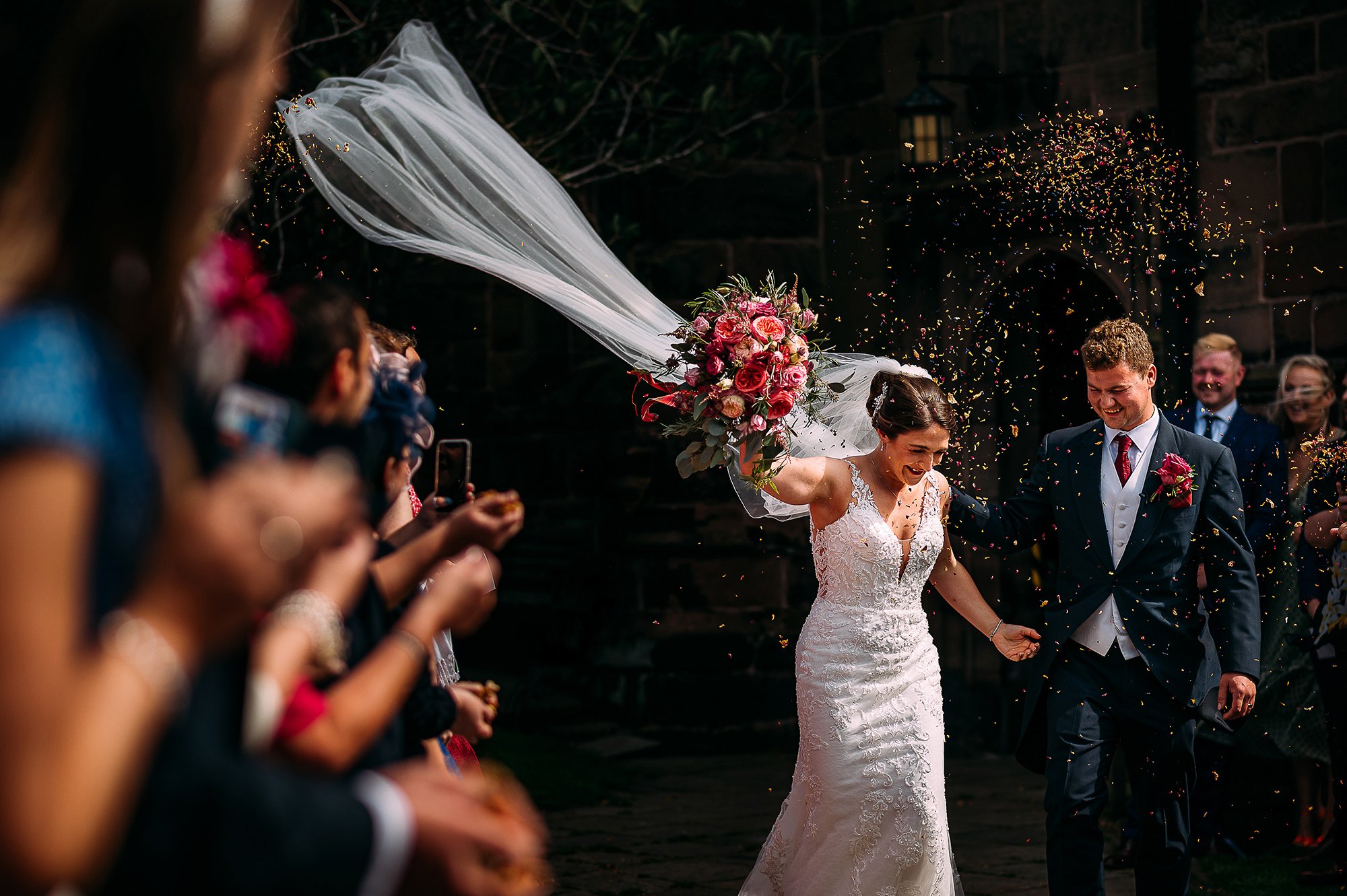  Brides veil blowing as they walk out of church through confetti. 