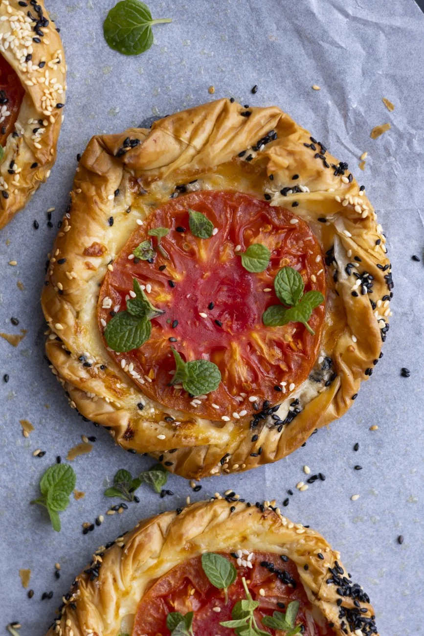 red heirloom tomatoes and basil leaves with melted cheese on a flaky crispy golden fillo pastry tart base