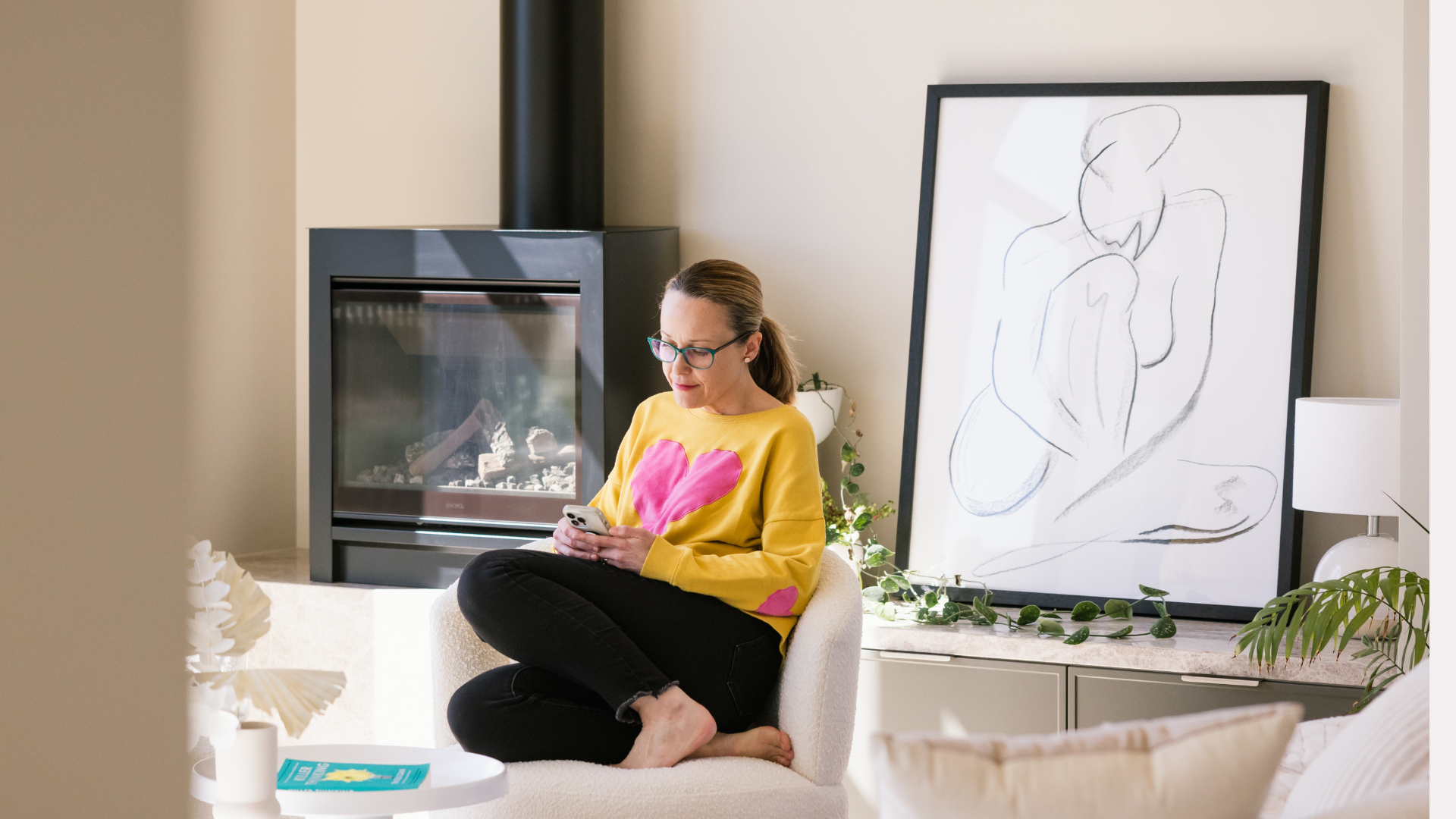 Erika is looking relaxed in a living room, on her phone. She's wearing a yellow jumper with a pink heart and has her feet tucked up under her. Small business marketing doesn't have to be so stressful.