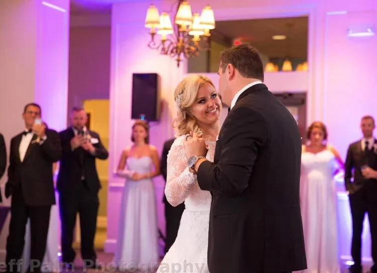 A bride and groom sharing an emotional first dance during a Rochester, NY wedding reception, featuring vibrant purple event uplighting provided by Sound Express Entertainment.