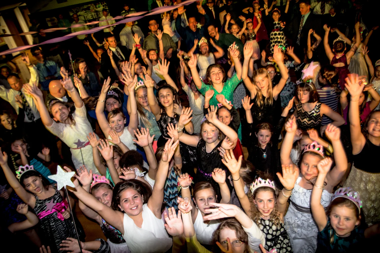 A large group of elementary school students with their hands in the air on a packed dance floor during a school event in Rochester, NY, provided by Sound Express Entertainment