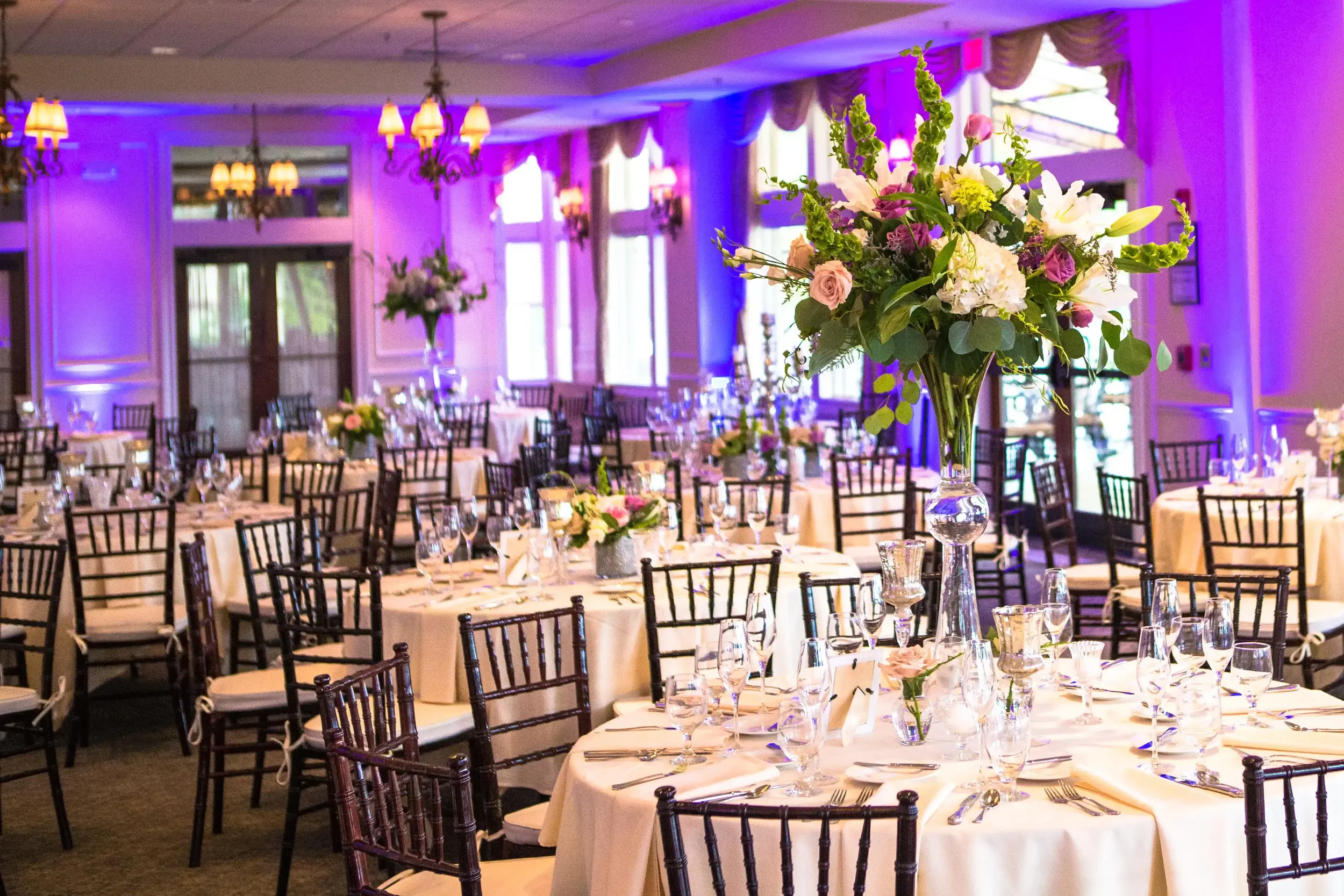Elegant wedding reception ballroom with purple uplighting and floral centerpieces provided by Sound Express Entertainment in Rochester NY