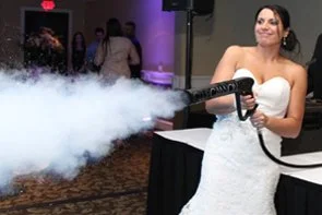 High-energy wedding party moment with CO2 cannons blasting white clouds over a dancing crowd.