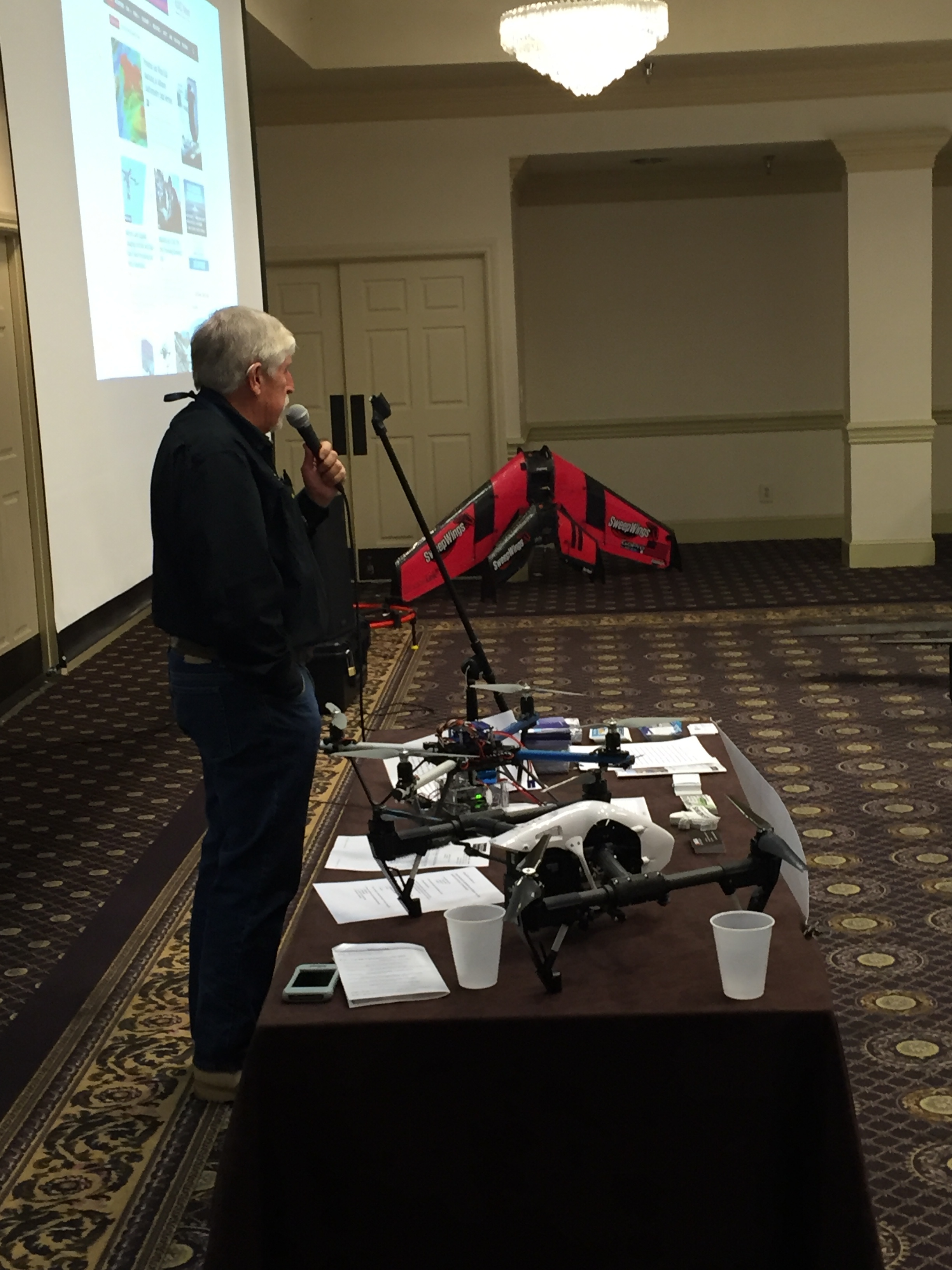 Bruce Parks, President of Drone Pilots Federation, provides an overview of the broad scopes and benefits of drone technology applications in our society. In the background are two flying wings that are designed, built, and flown by one of the other speakers at the event.