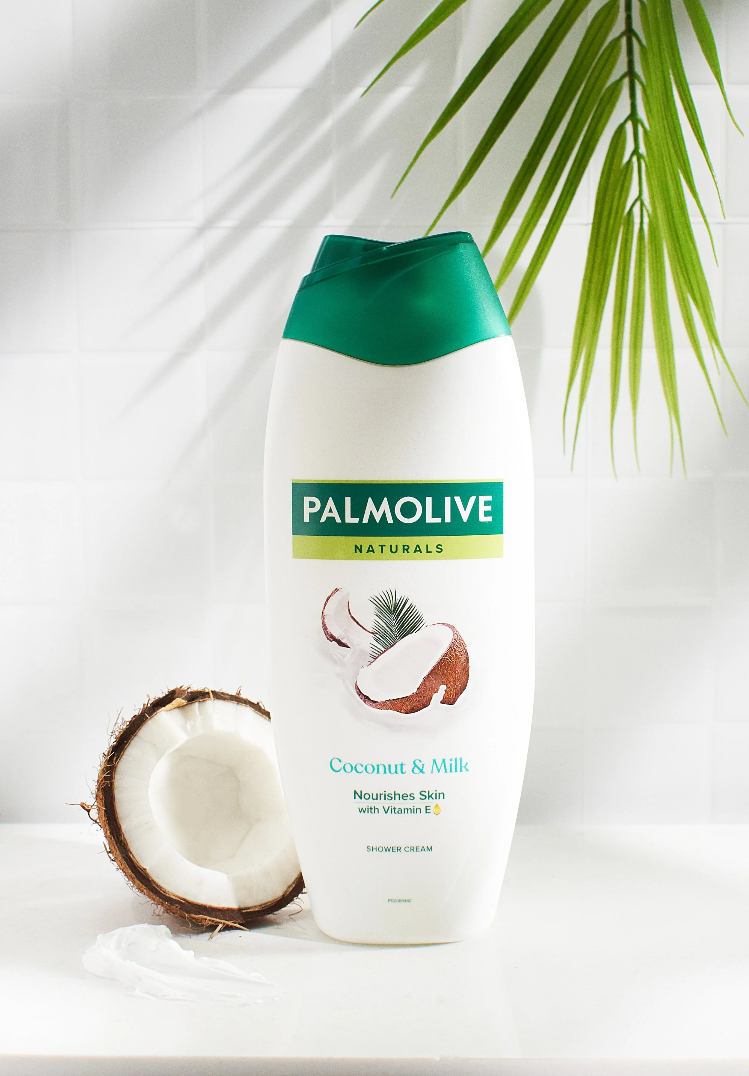 A bottle of Palmolive Naturals Coconut & Milk shower cream with coconut pieces beside it, and a sliced open coconut in the foreground, with a green plant in the background. Product photography UK and London, lifestyle photography, brand photography.