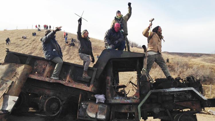 Protesters against the Dakota Access oil pipeline stand on a burned-out truck near Cannon Ball, N.D., on Nov. 21. (James MacPherson / Associated Press) via LA Times