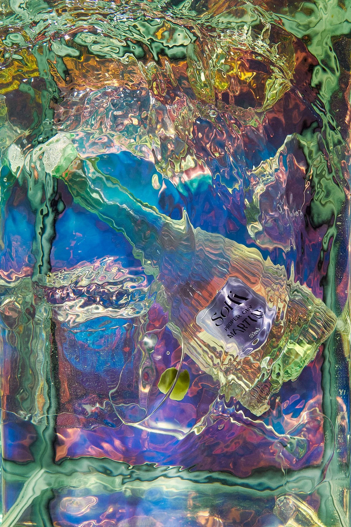 Close-up of a shattered and distorted plastic bag with colorful reflections and a label that reads 'Sodi Proper Gin MARTINI' amid a chaotic abstract background.
