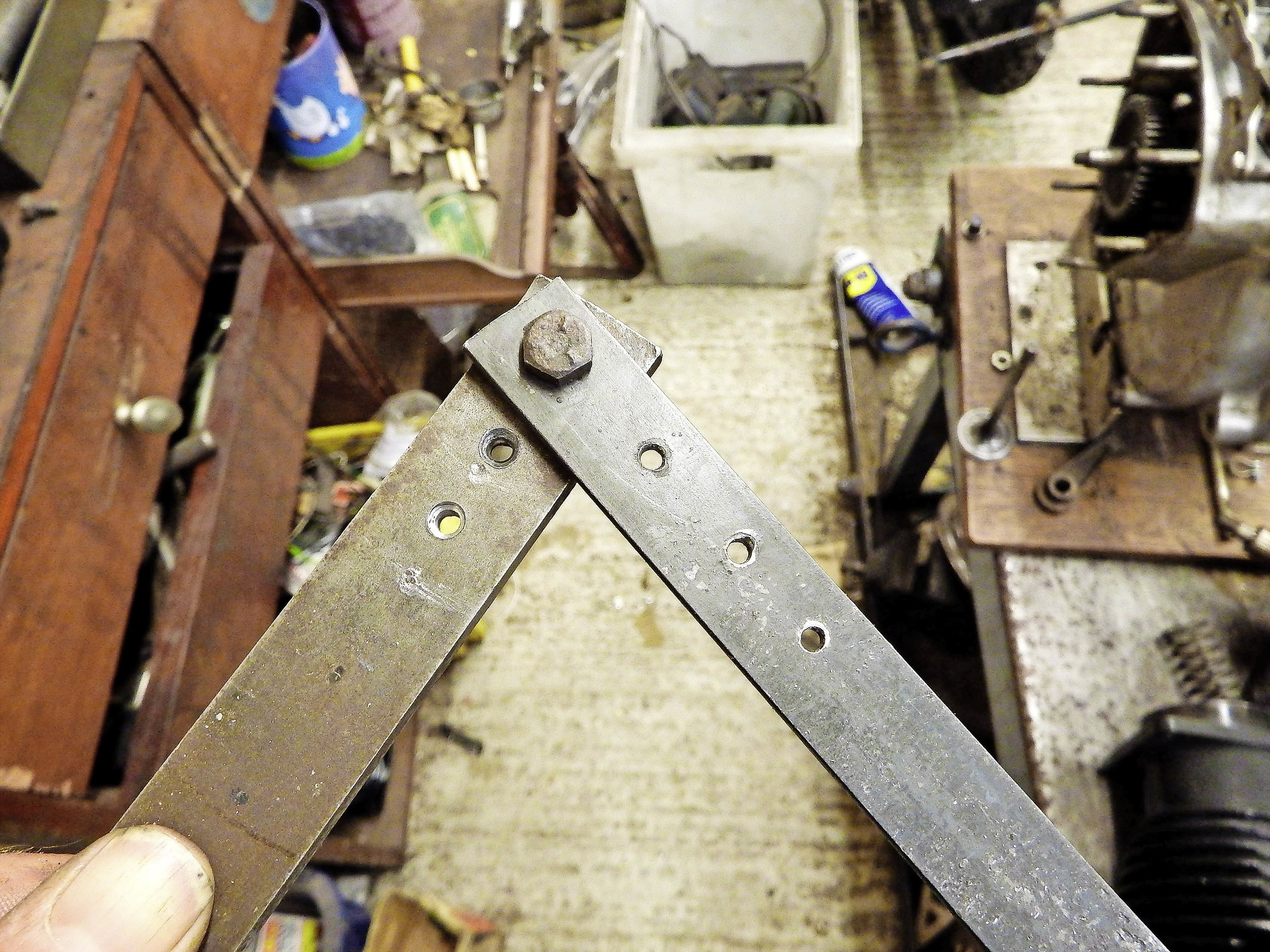 1. First you need some steel strip, drilled to accept the spoke with a countersink to accommodate the head. The thickness of the strip gives the depth of bend, so I have two to choose from. Join them at one end.