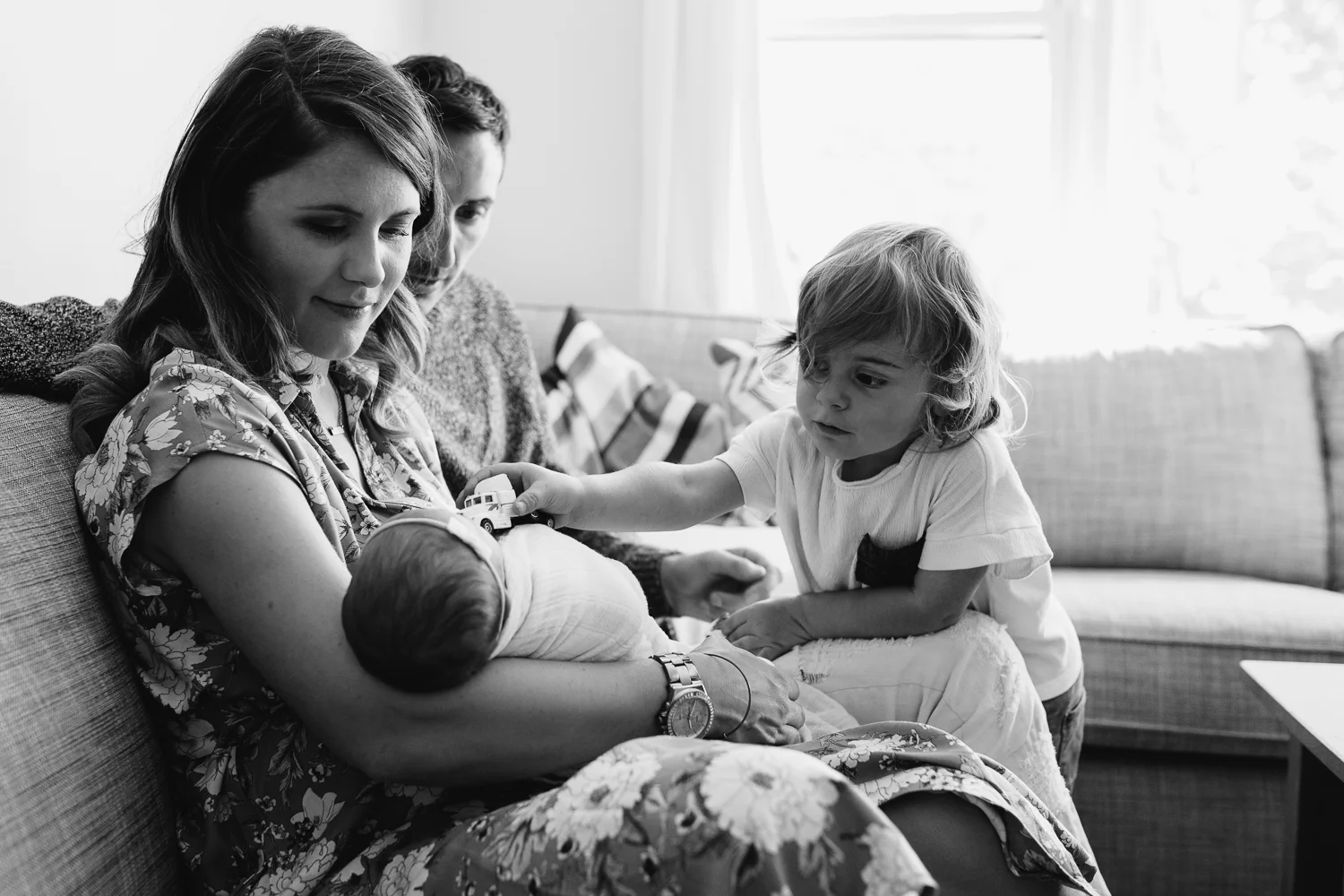 mother holding 1 week old baby girl while 3 year old big brother drives toy truck on little sister - Markham family photos