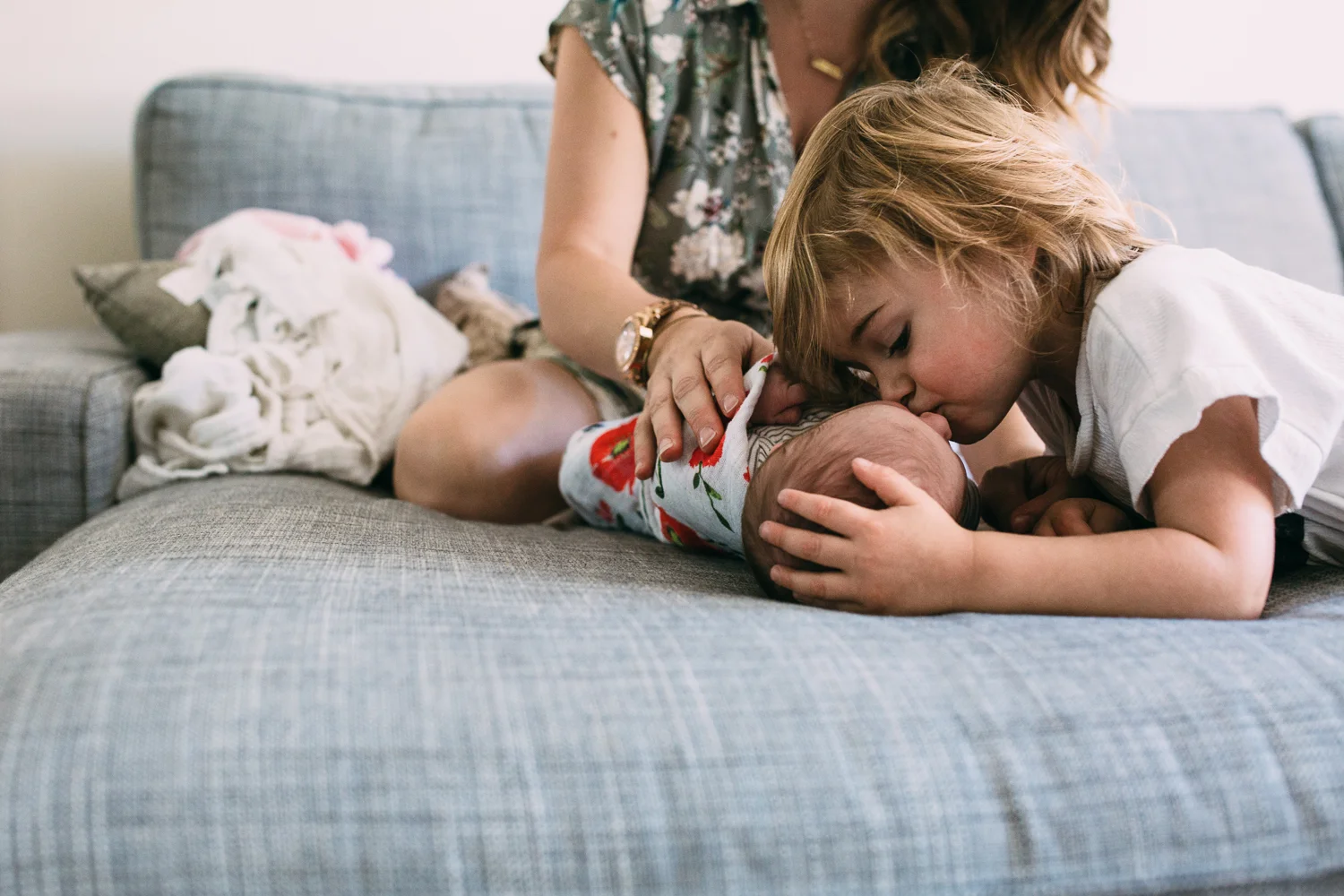 3 year old toddler boy kissing 1 week old baby sister on head while mom watches - Newmarket family photos