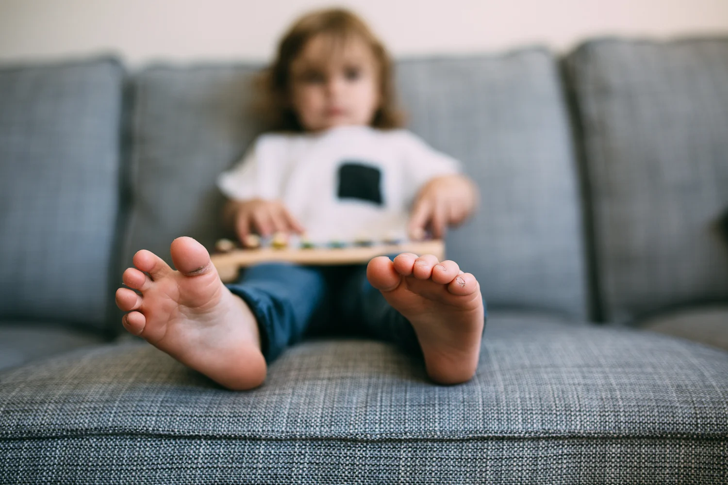 3 year old toddler boy sitting on couch playing on toy xylophone with feet sticking out - newmarket child photography