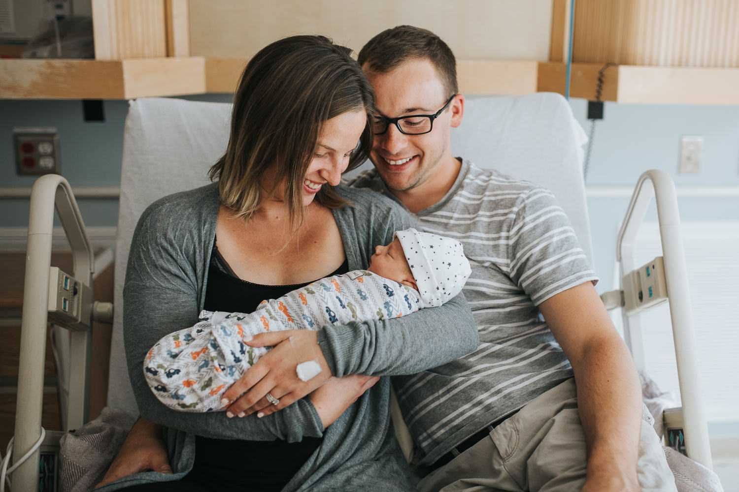 family of three sitting on hospital bed looking at newborn baby boy - Newmarket Fresh 48 photography