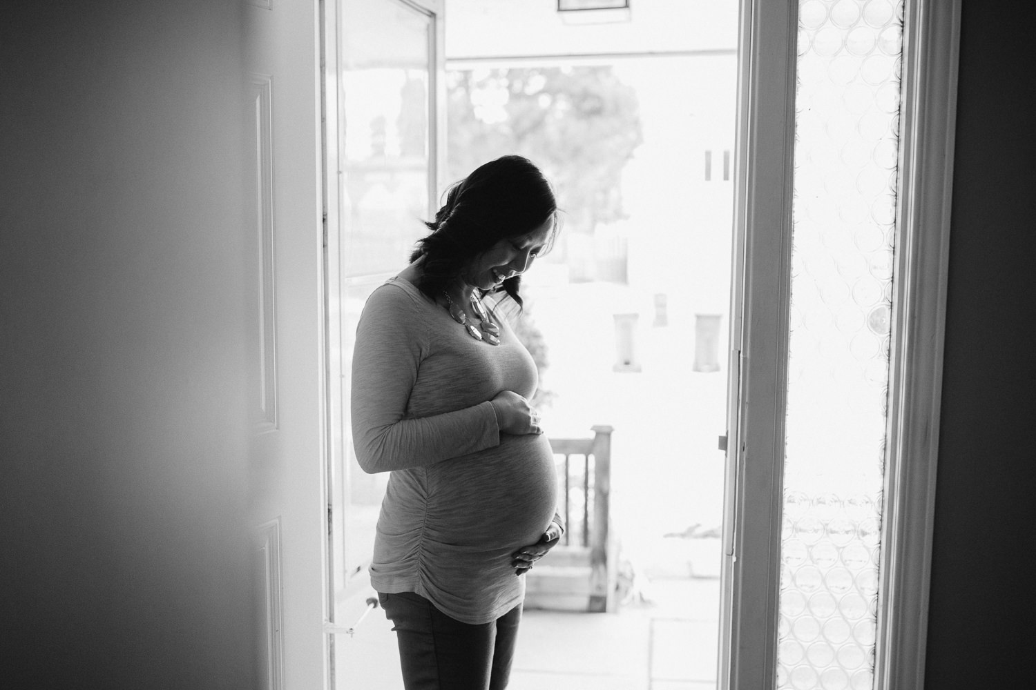 pregnant woman with short brown hair holding baby bump standing in doorway - Stouffville in-home photography