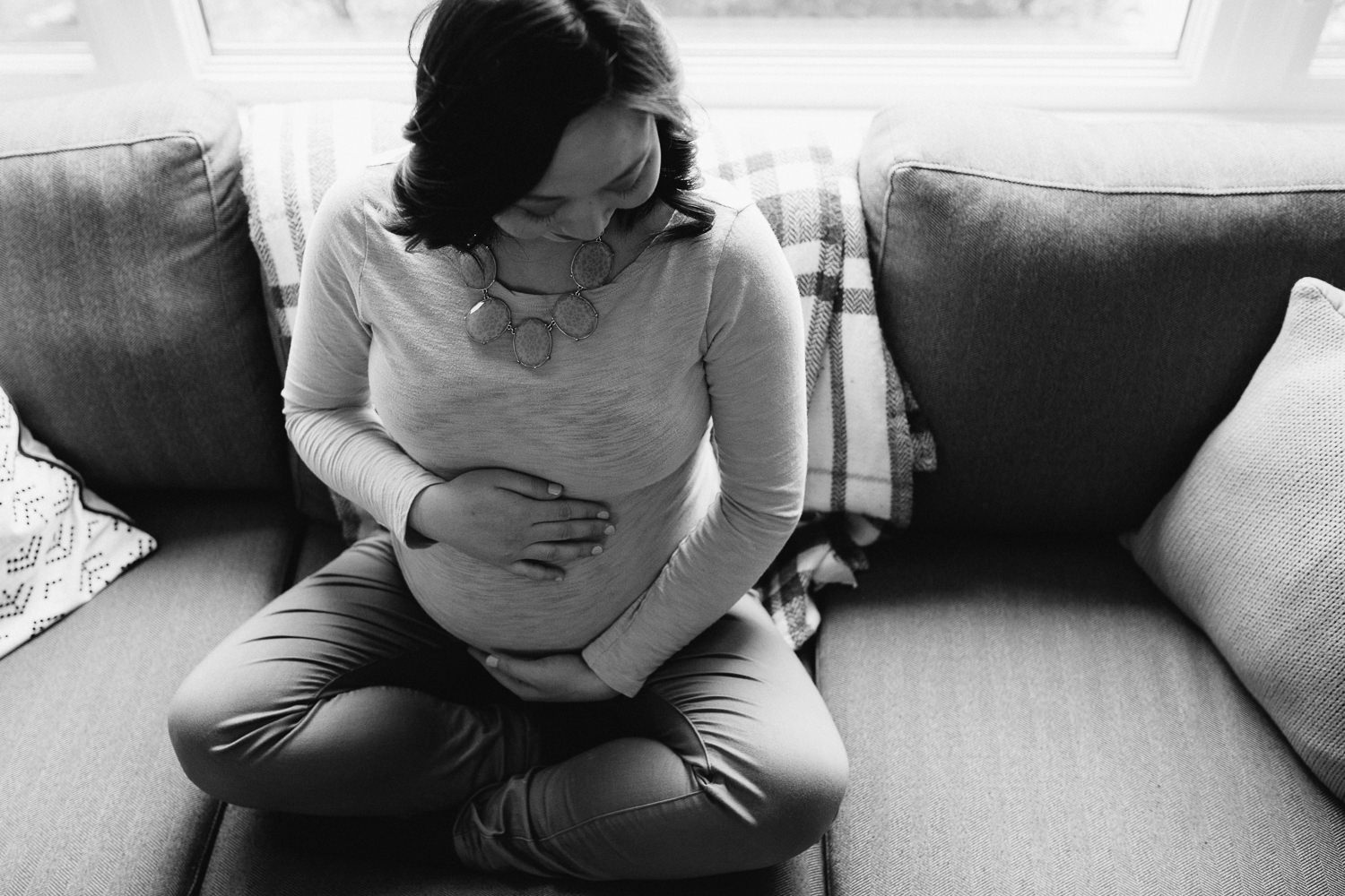 pregnant woman sitting on couch holding baby bump - markham in-home photography