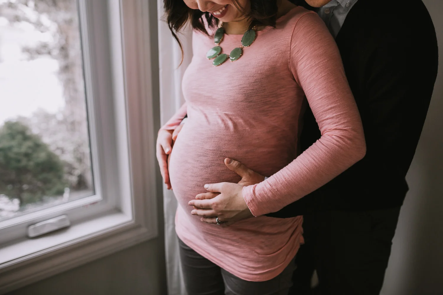 husband embraces pregnant wife, holding baby bump - Markham Lifestyle Photography