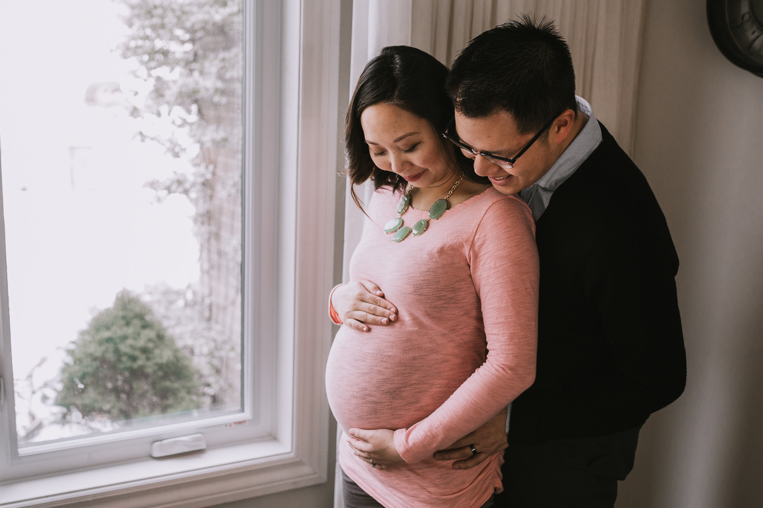 husband embraces pregnant wife, looking at baby bump - Markham Lifestyle Photography