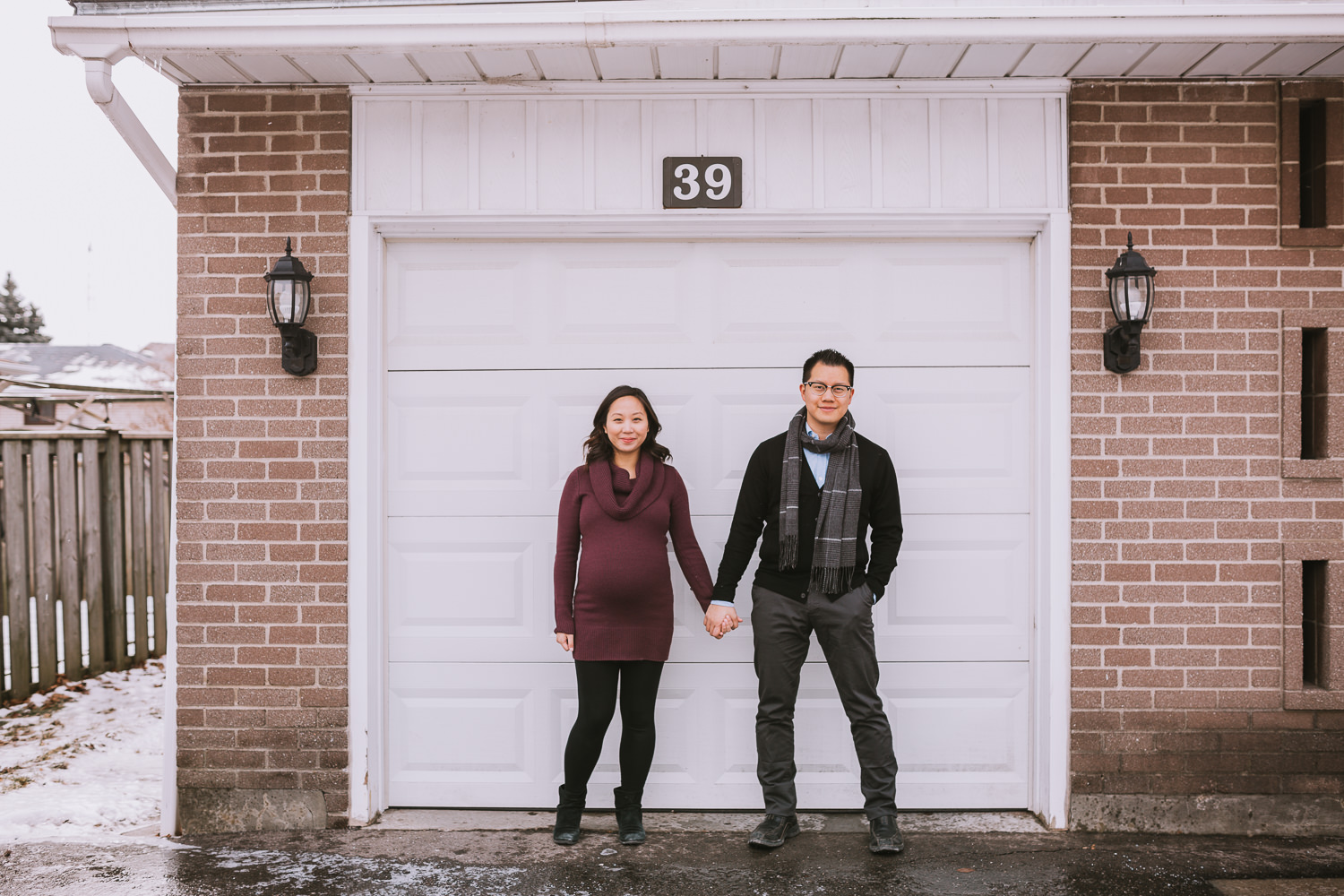 couple expecting first baby holding hands standing on front of garage door - Uxbridge lifestyle photography