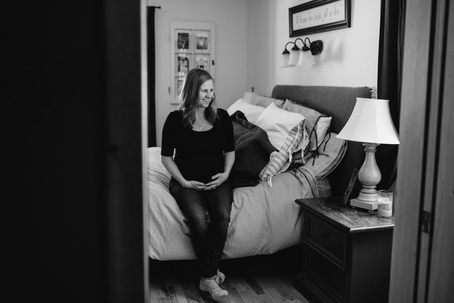 pregnant mom to be sitting on side of bed looking at baby bump - markham in-home photography