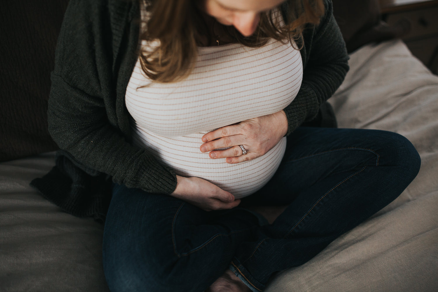 pregnant mom to be sitting on bed holding baby bump - Stouffville in-home photography