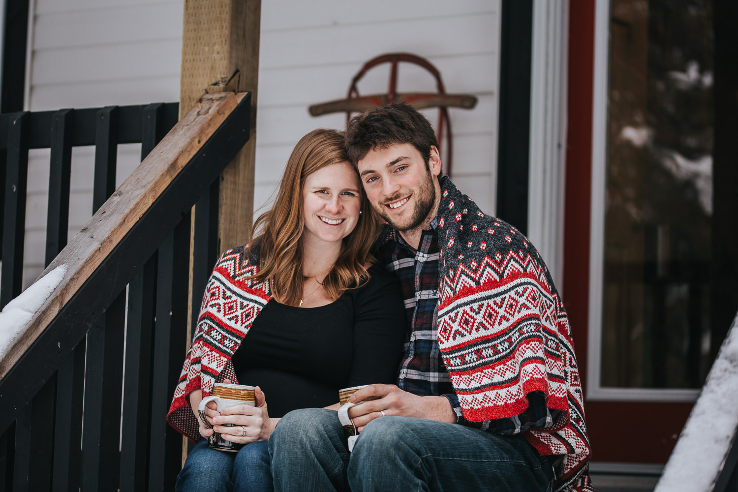 parents to be sitting on front porch steps wrapped in blanket looking at camera  - Uxbridge lifestyle photography