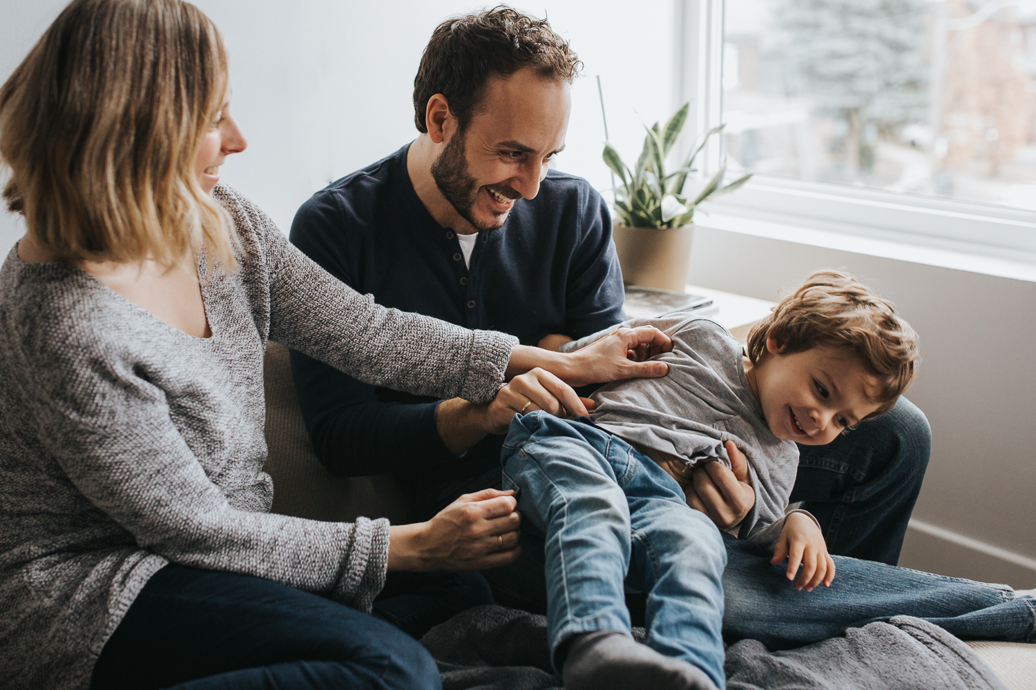 family of 3 with toddler boy and pregnant mom tickling on couch - markham family photography