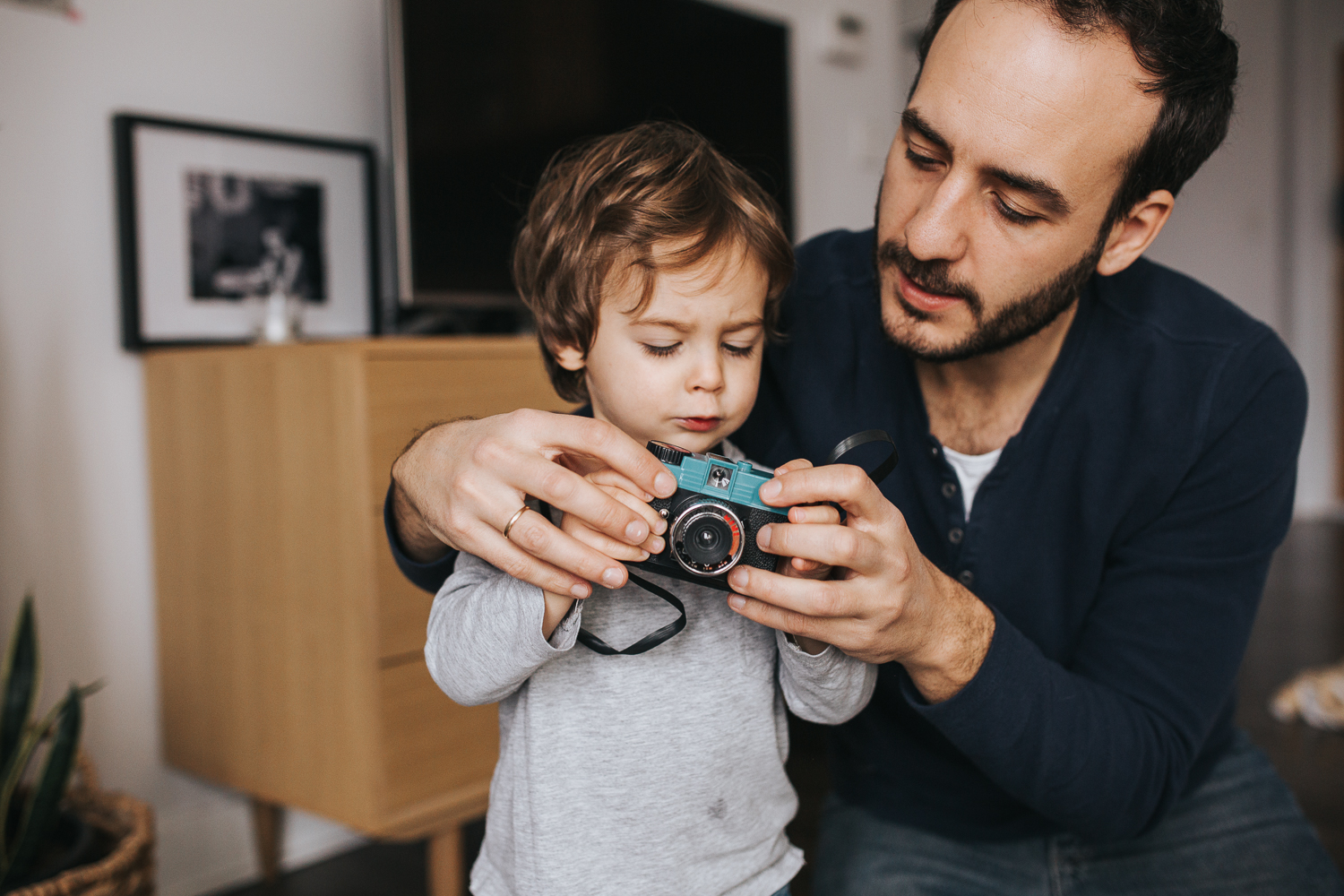 father helping 2 year old toddler boy with toy camera - newmarket family photography