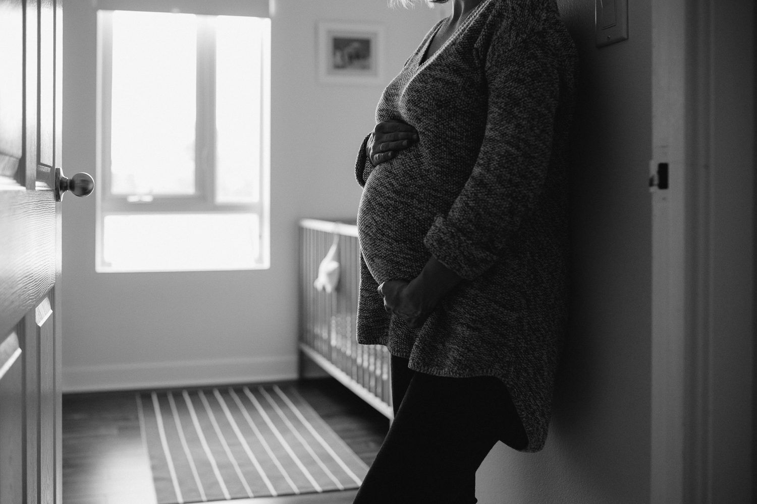 pregnant woman leans against nursery doorway, hands on baby bump - newmarket in-home lifestyle photography