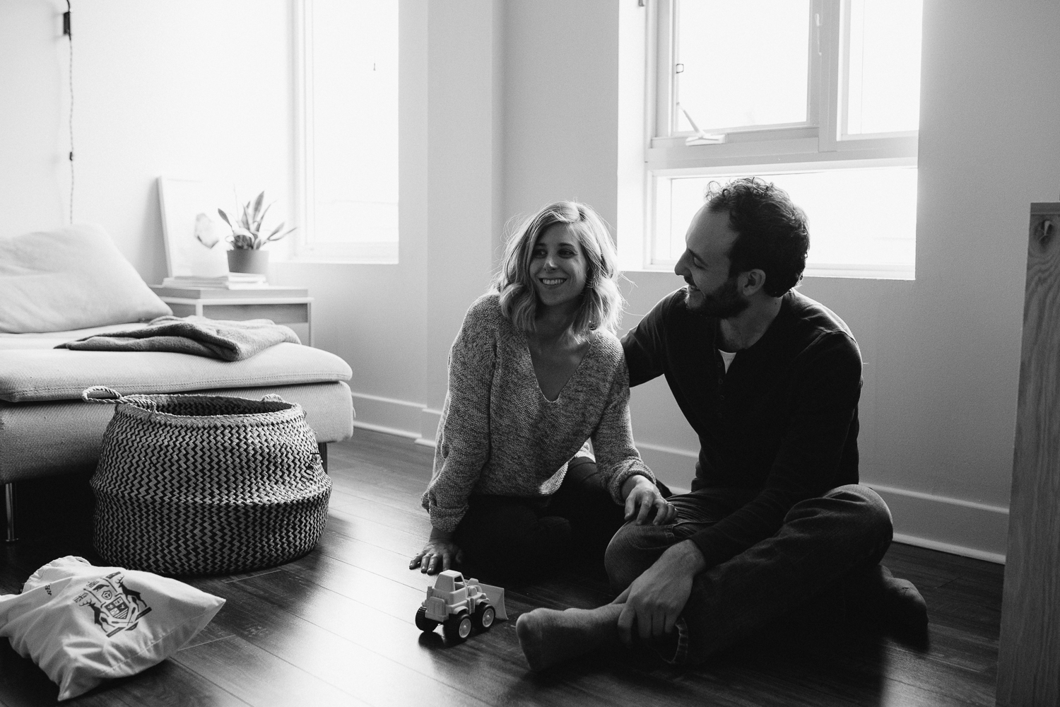 mom and dad sit on floor watching son play in the distance - stouffville in-home family photography