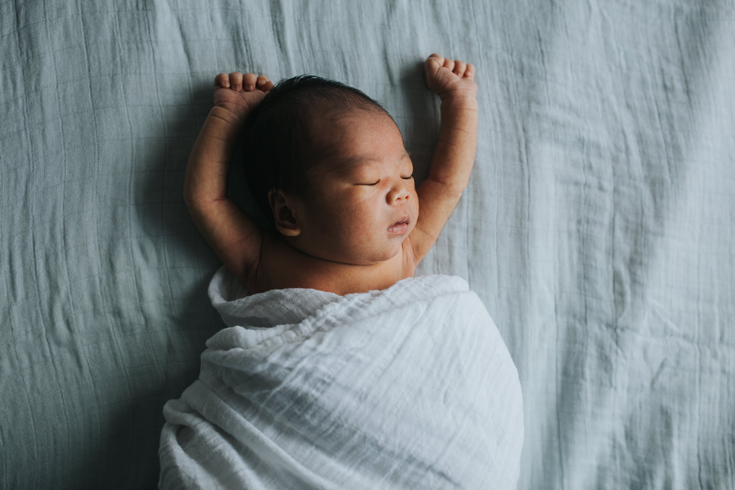newborn baby boy sleeping and lying on bed with hands in air - Markham lifestyle photography