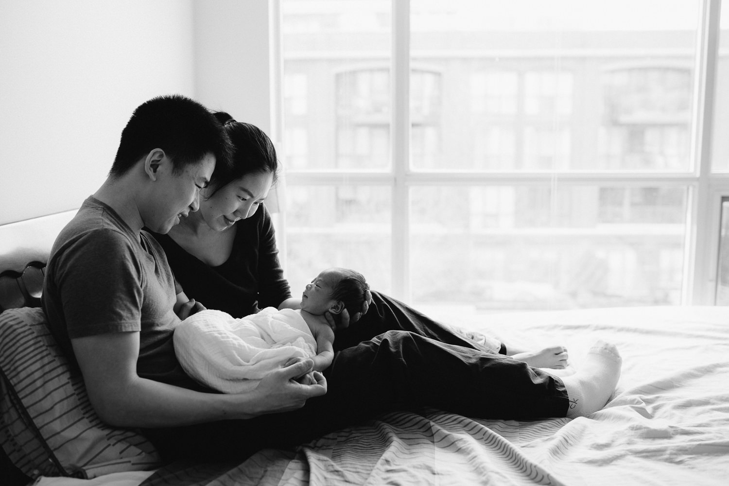 new parents snuggle and look at 2 week old baby boy while sitting in bed - Barrie lifestyle photography