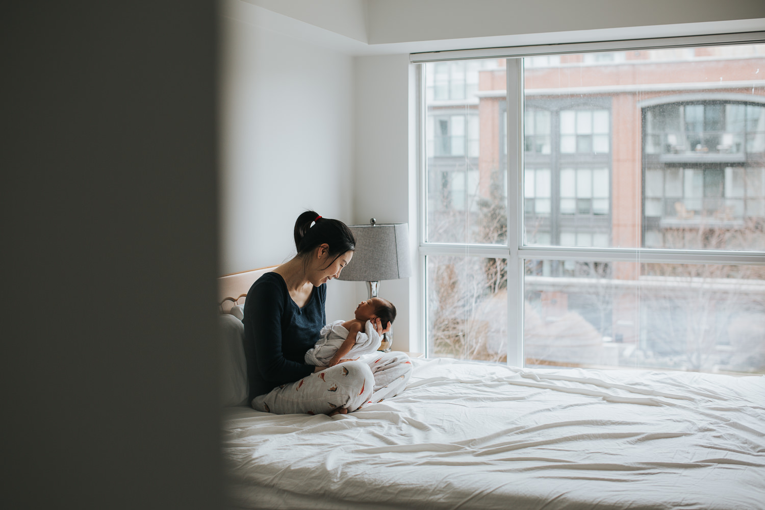 first time mom holding and looking at 2 week old baby boy in master bedroom - Barrie lifestyle photos