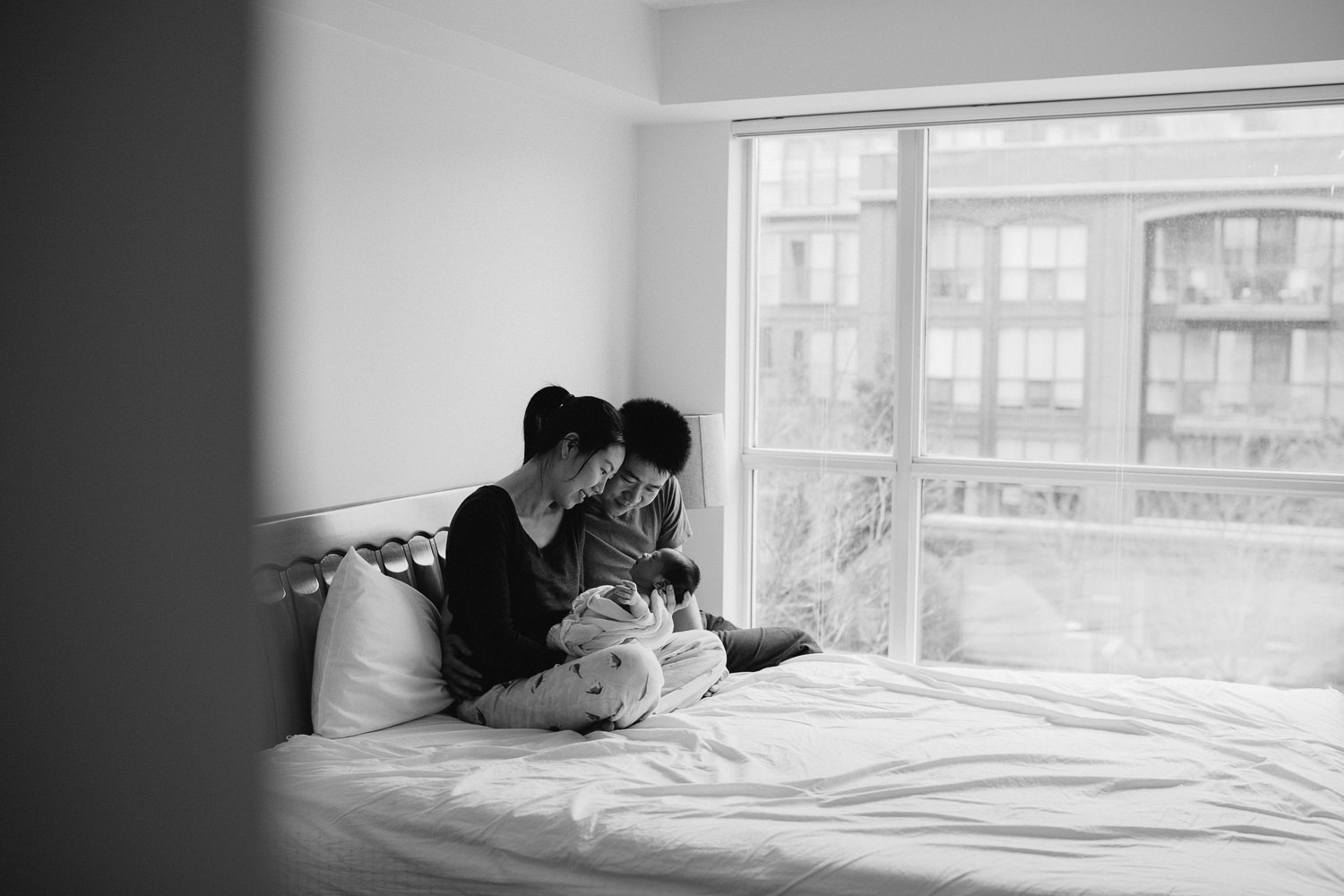 new parents snuggle and look at 2 week old baby boy while sitting in bed - Markham lifestyle photography