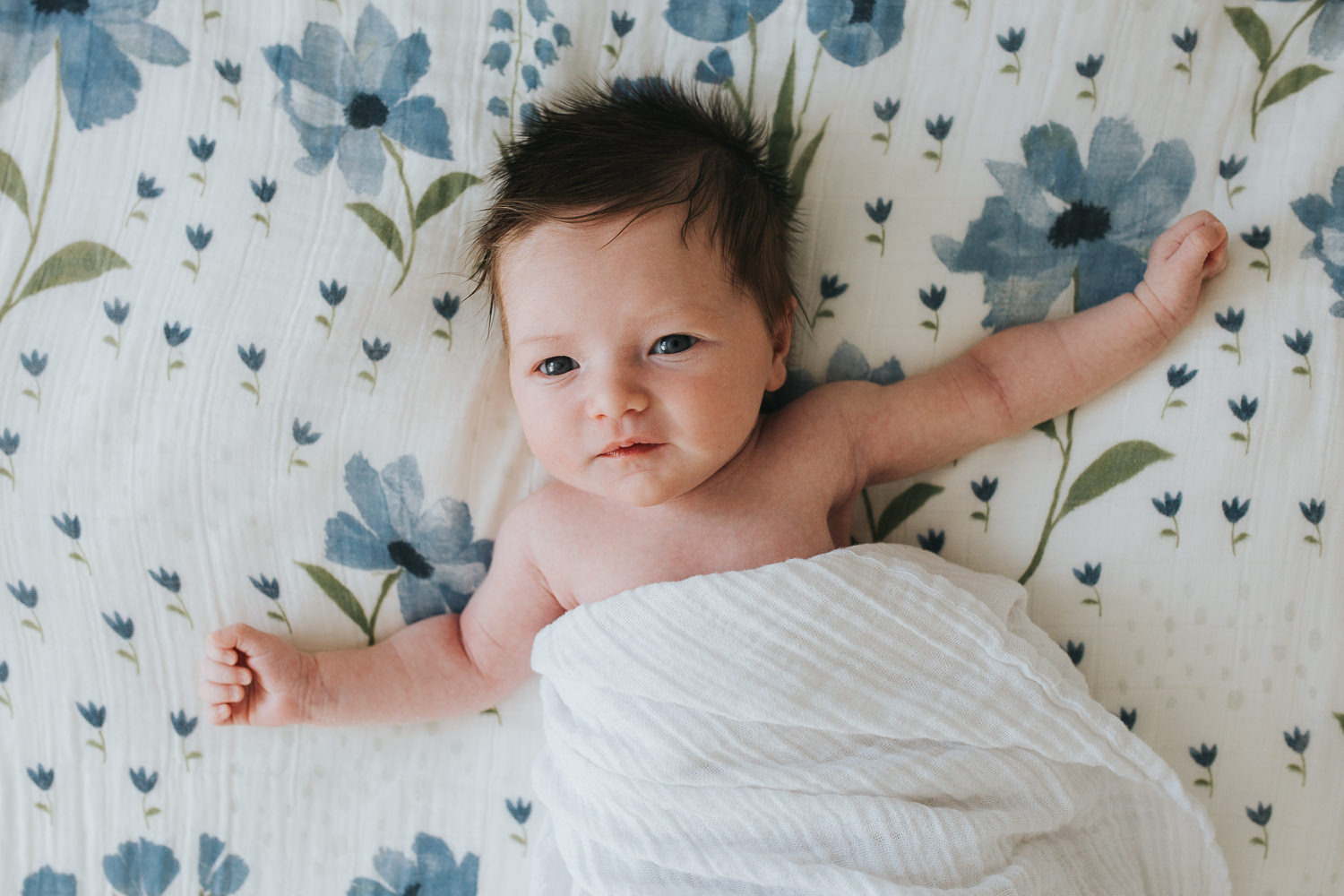 2 week old baby girl with lots of dark hair lying on bed looking at camera - Stouffville in-home photography 