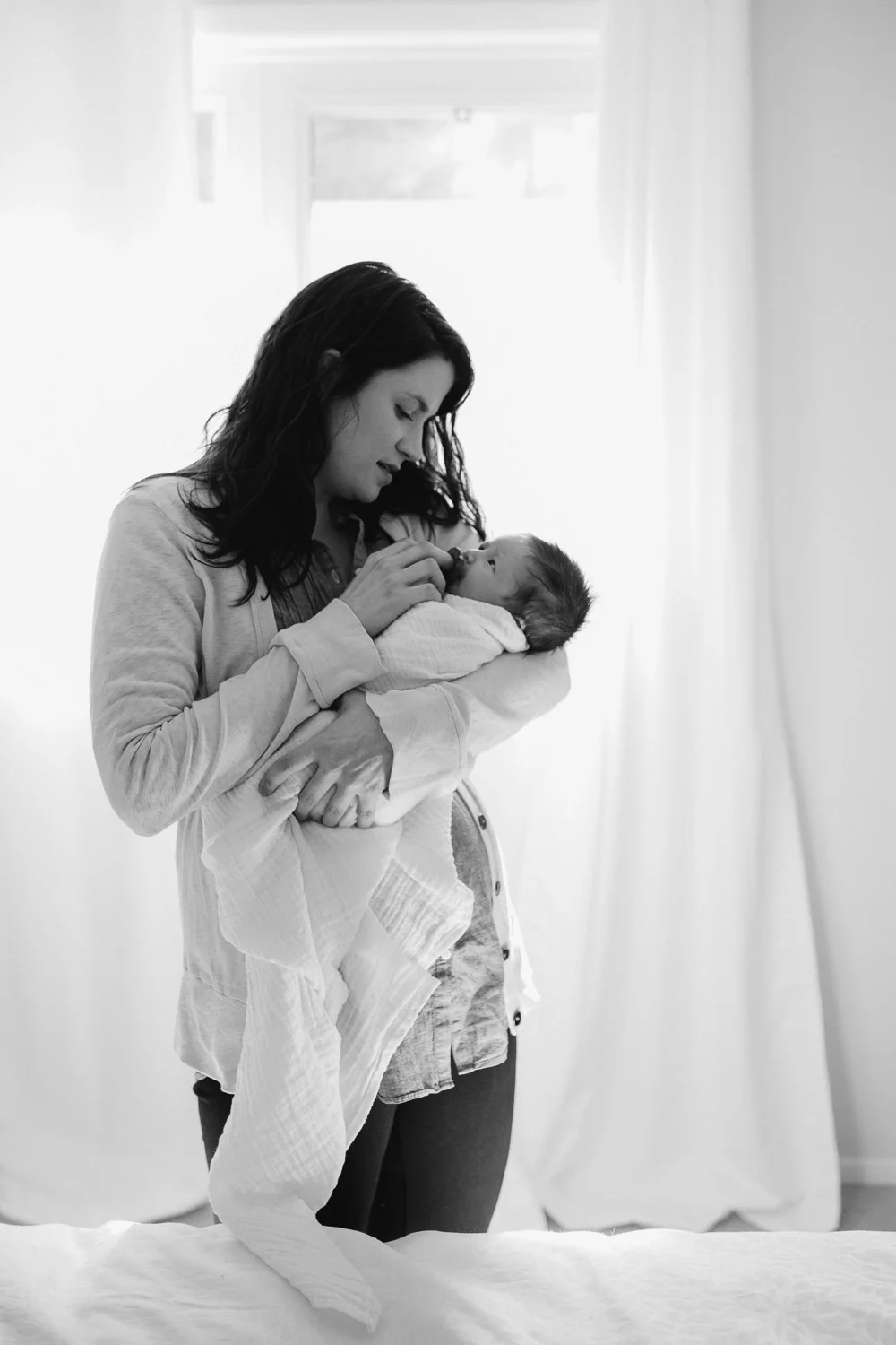 mother holding and looking at swaddled 2 week old baby girl - Barrie in-home photography 