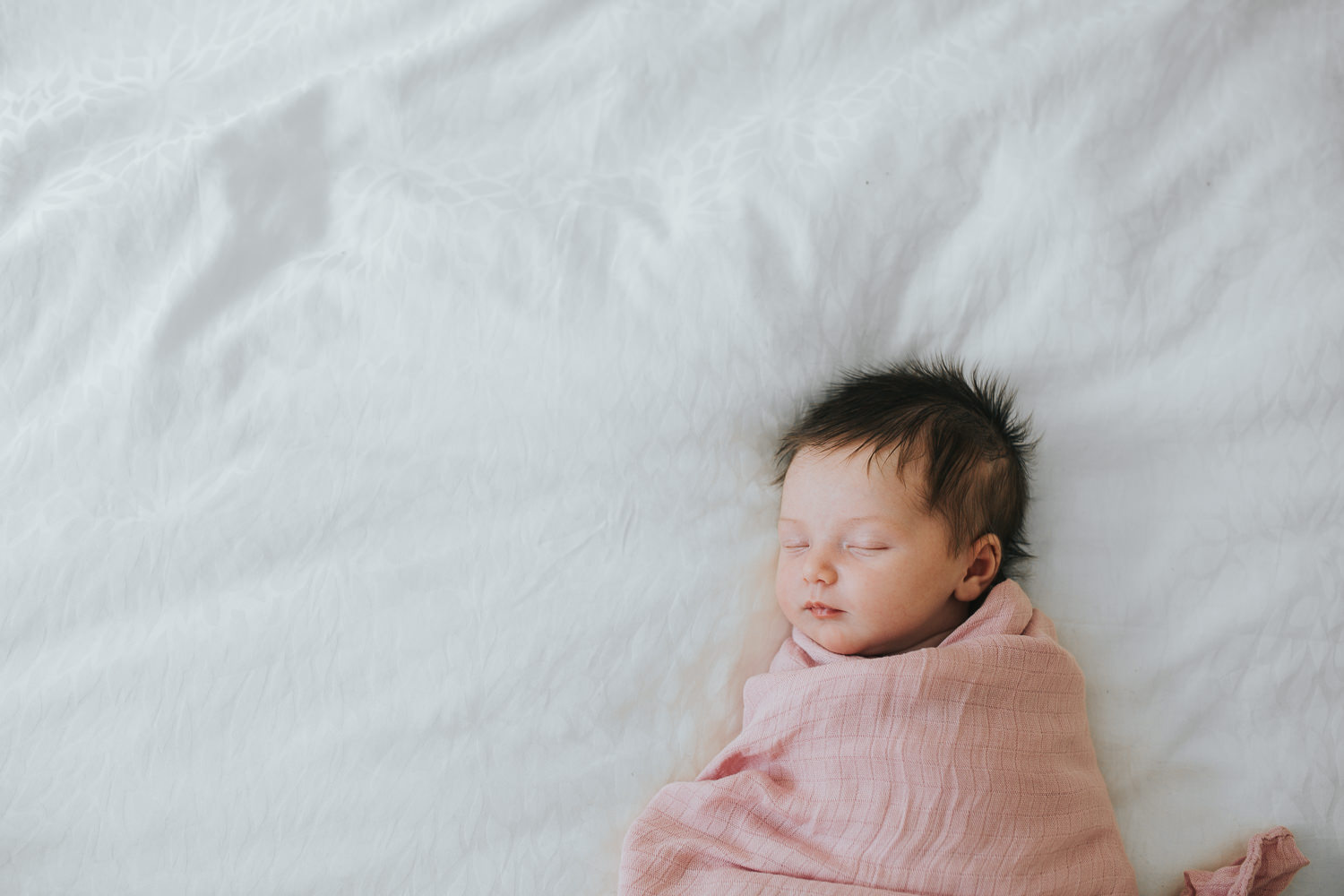 2 week old baby girl with lots of dark hair in pink swaddle sleeping on bed - Stouffville in-home photos