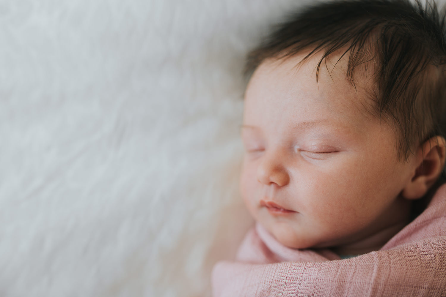 2 week old baby girl with lots of dark hair in pink swaddle sleeping on bed - Markham in-home photos