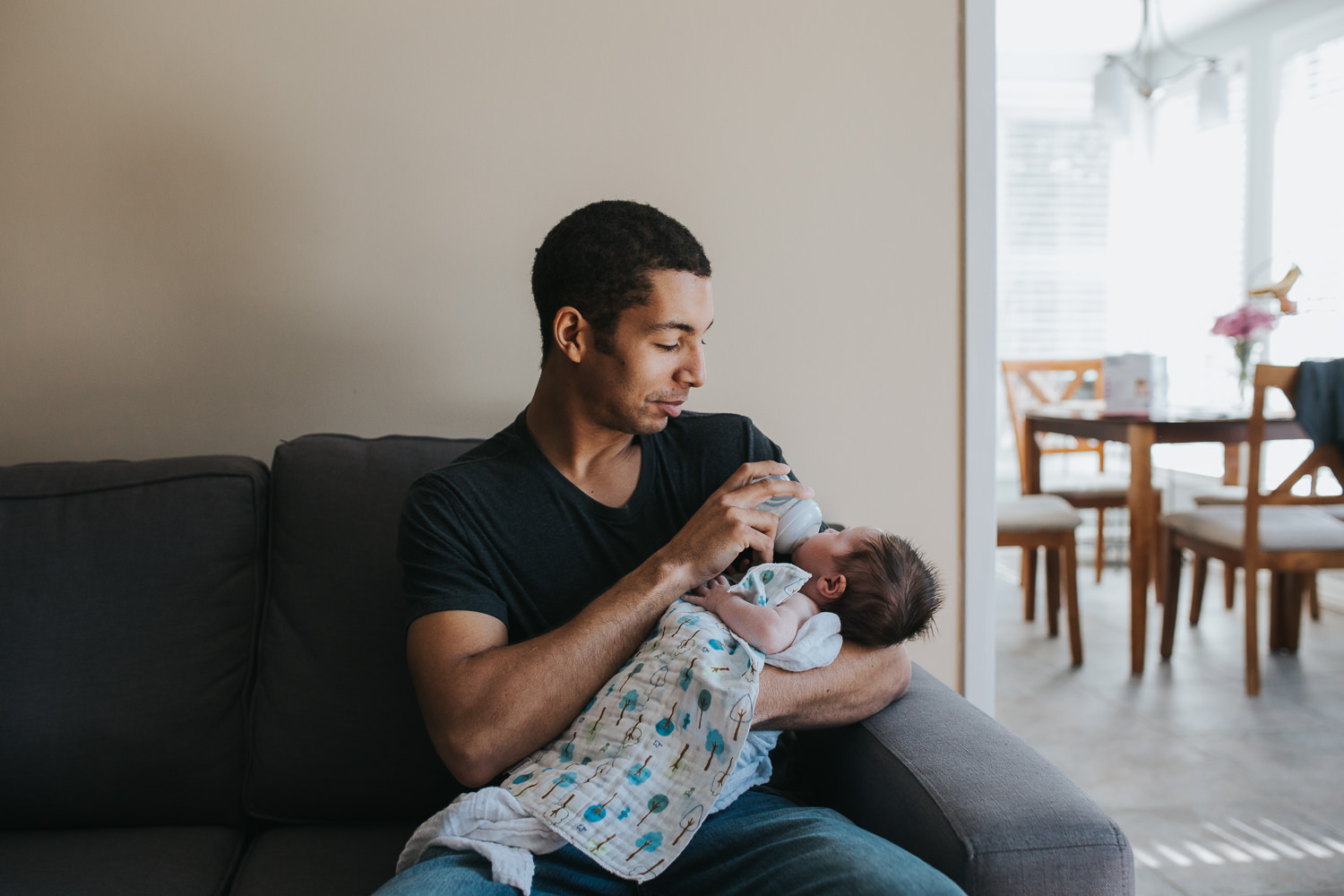 new dad holding 2 week old baby girl and feeding her bottle on couch - Newmarket lifestyle photos
