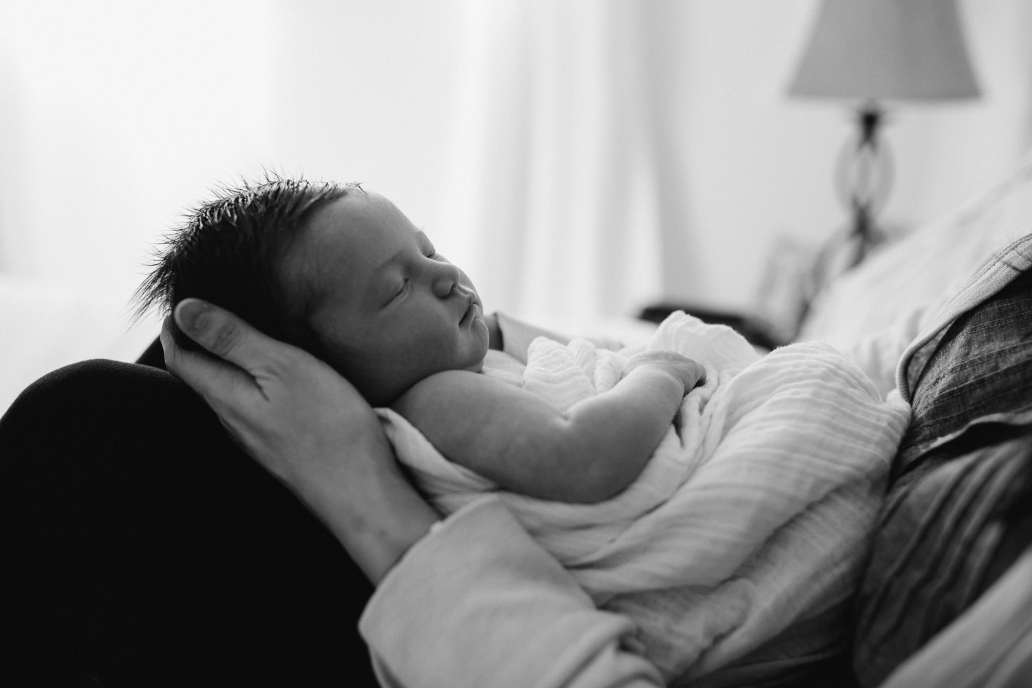 mom sitting on bed holding 2 week old baby daughter who is sleeping - Newmarket lifestyle photography session